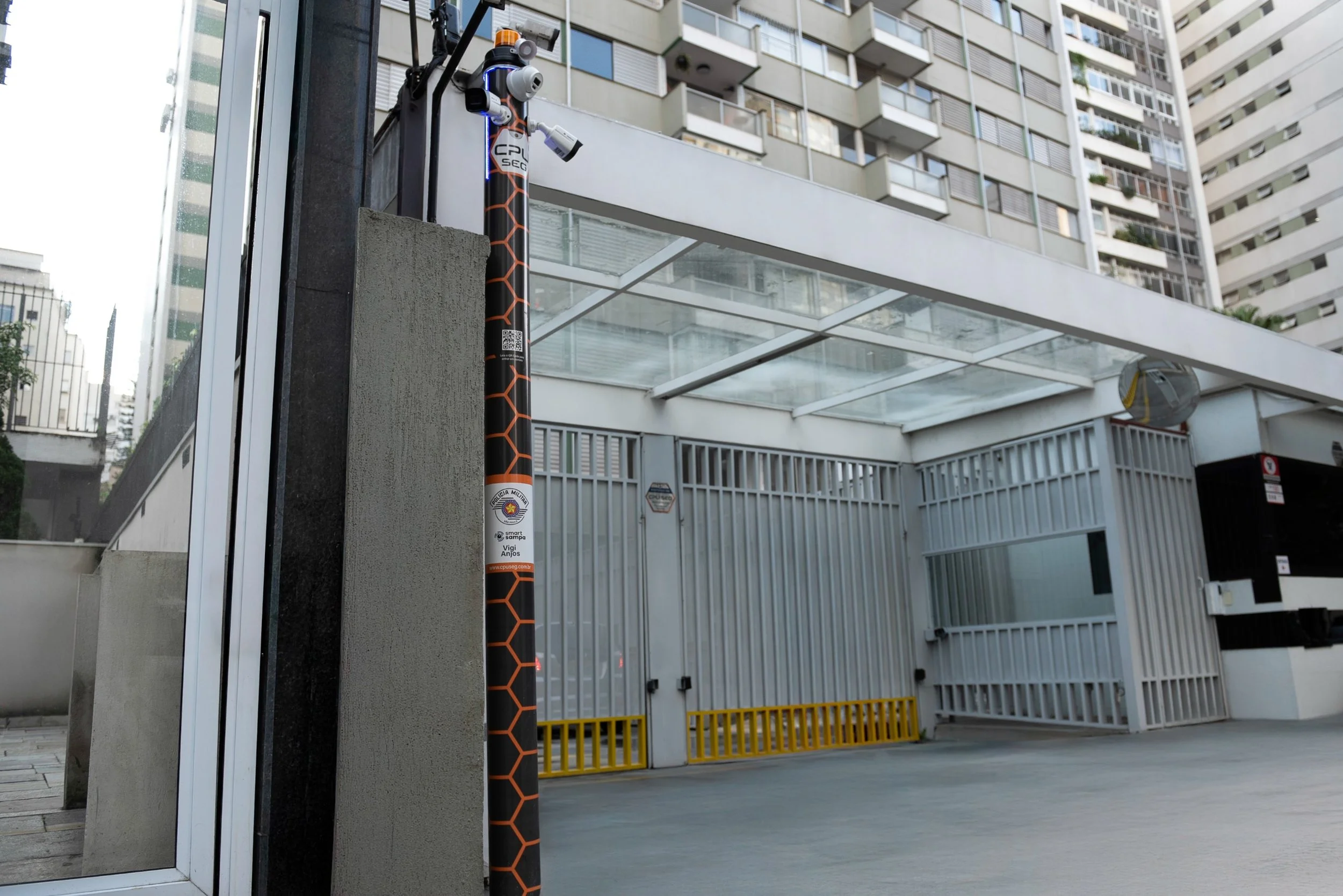 A security camera pole with multiple cameras and a sign in front of a modern residential building