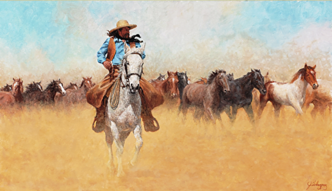 A cowboy riding a white horse in a herd of running horses in a dusty field under a partly cloudy sky.