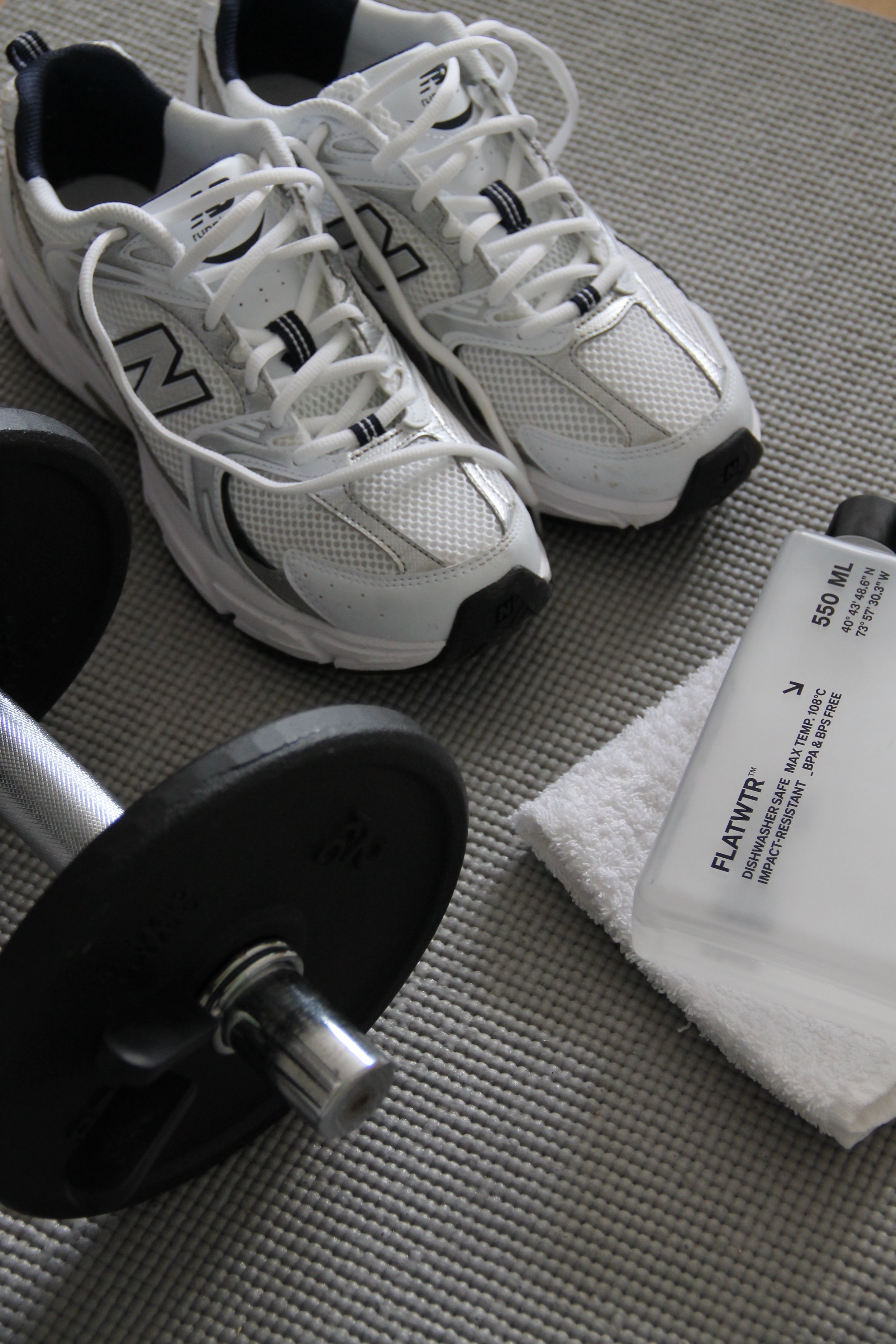Pair of white New Balance running shoes, a black dumbbell, and a bottle of dish soap on a textured surface.