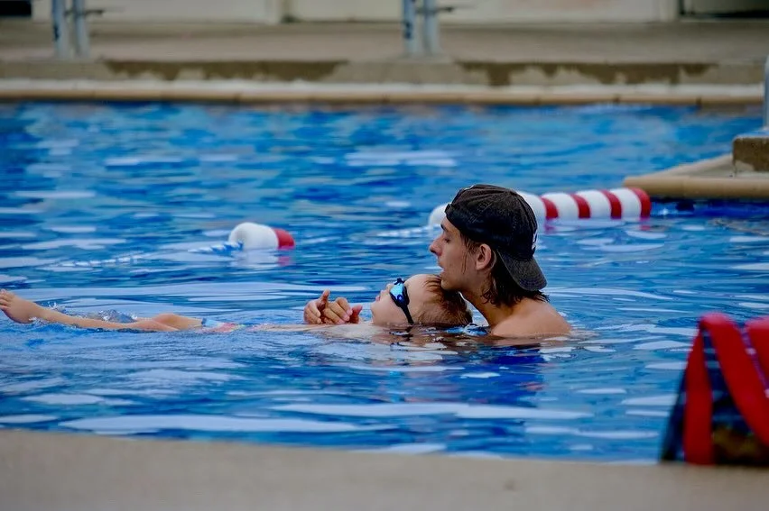 Adult male swimming instructor helping a young girl in a swimming pool.