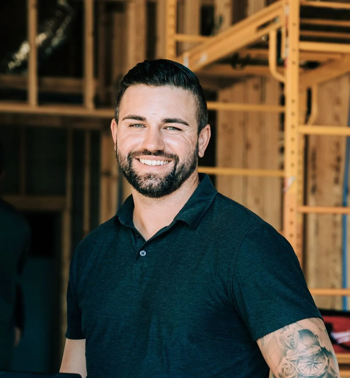 John smiling in an indoor setting with wooden shelves and unfinished walls.