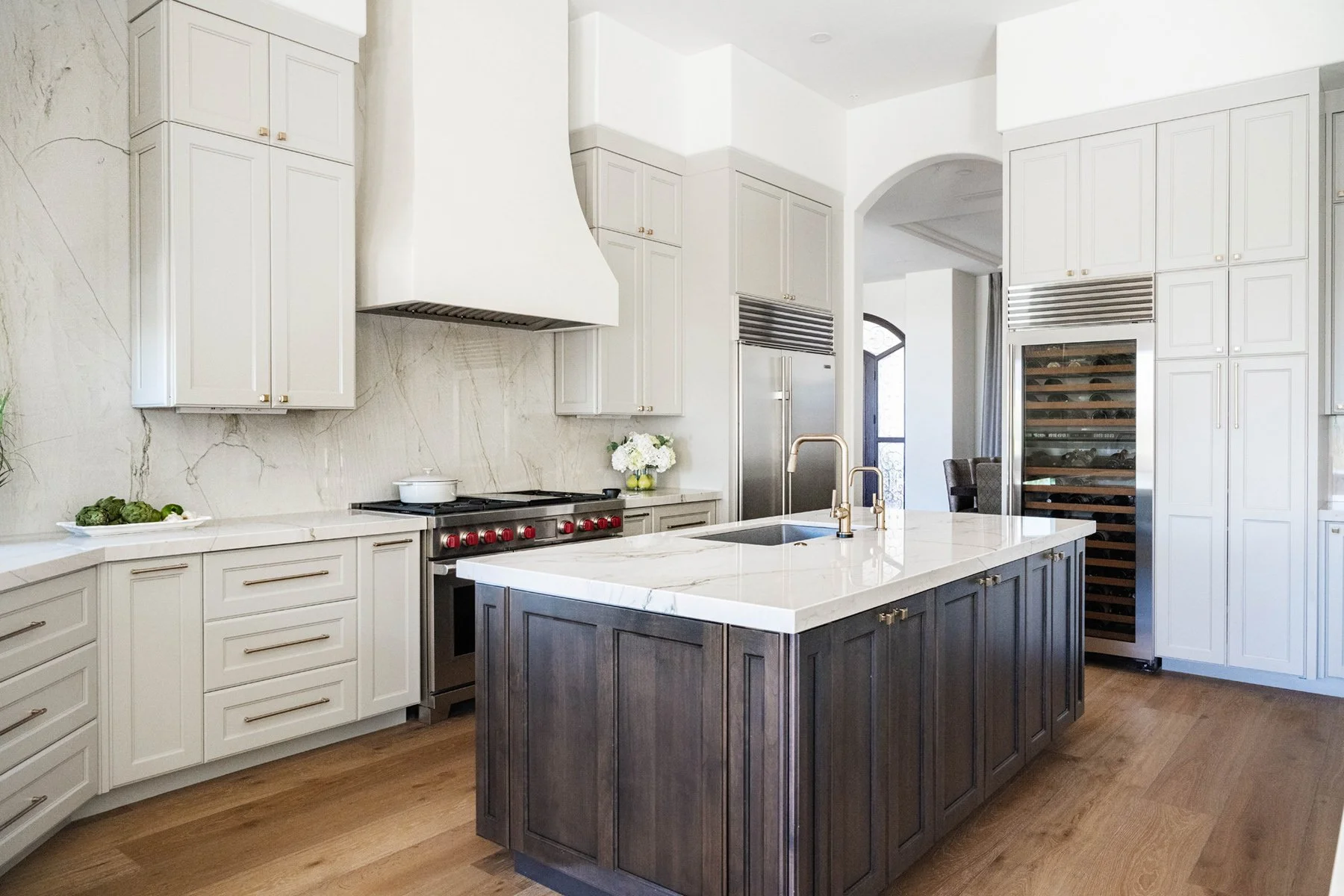 Arizona home kitchen with soft greige cabinets, white plaster range hood, quartzite backsplash, and dark stained wood island