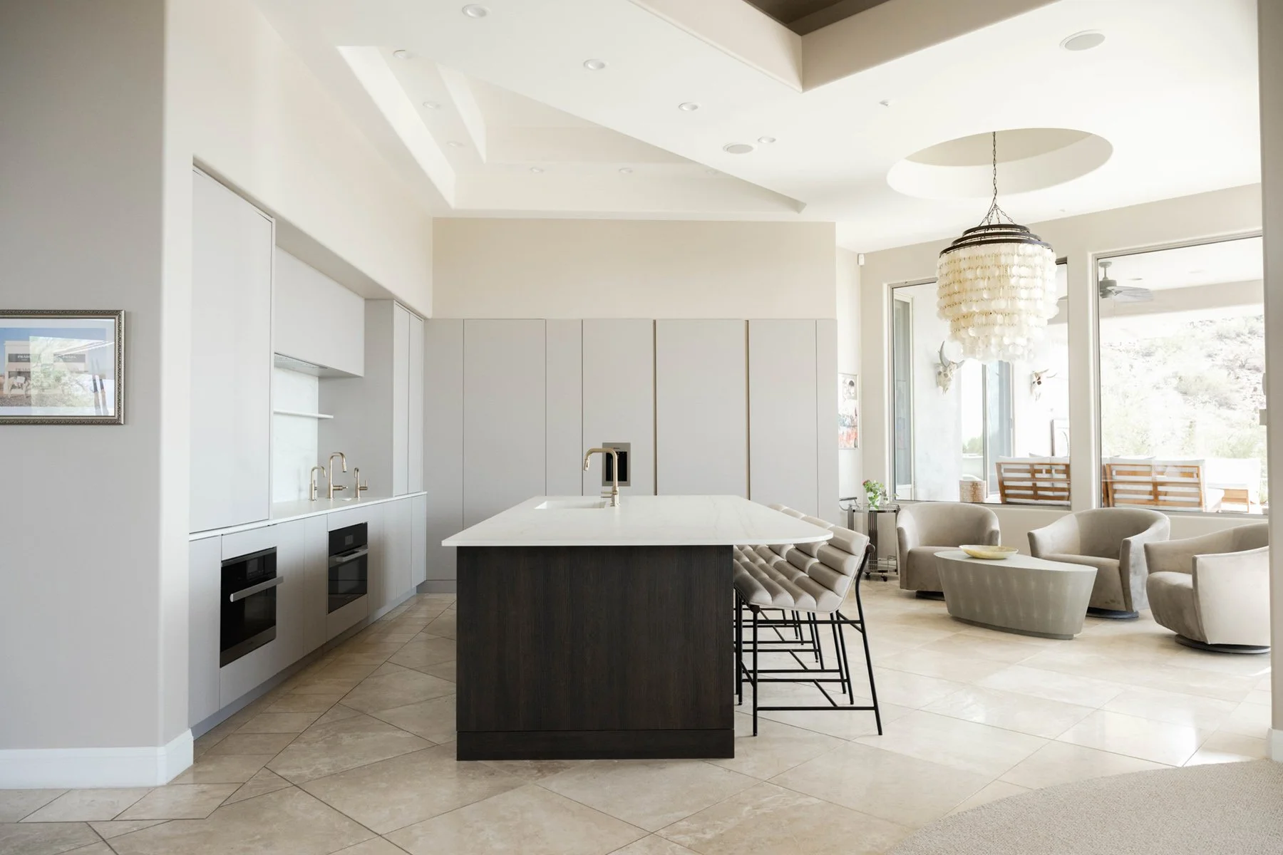 Modern Arizona kitchen with light gray flat-panel cabinets, dark wood island, capiz chandelier, and travertine floors in natural light