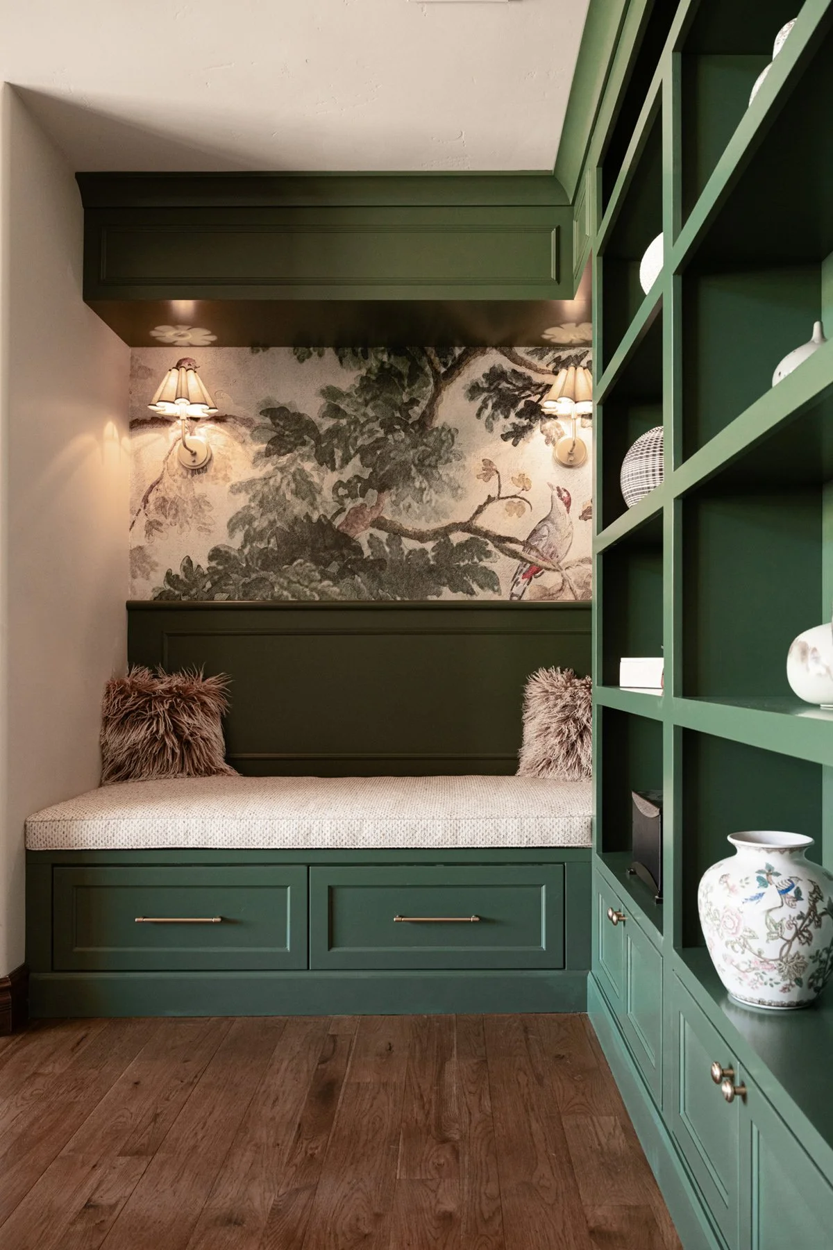 Built-in reading nook with deep green paint, bird and tree mural, brass sconces, and green shelves showing calming paint colors for home