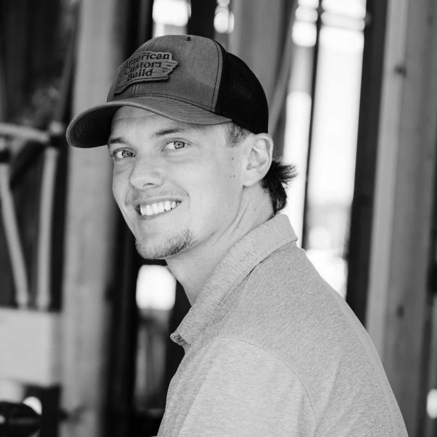 Aaron, smiling and wearing a baseball cap and a casual shirt, in a black-and-white photo.