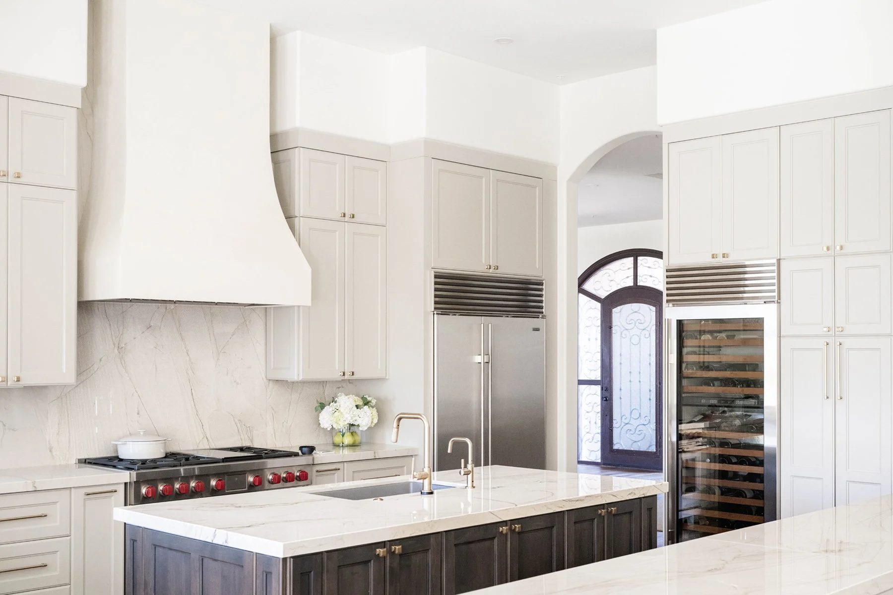 Custom kitchen with warm greige painted cabinetry, stained wood island, brass faucet, and built-in wine fridge on oak floors