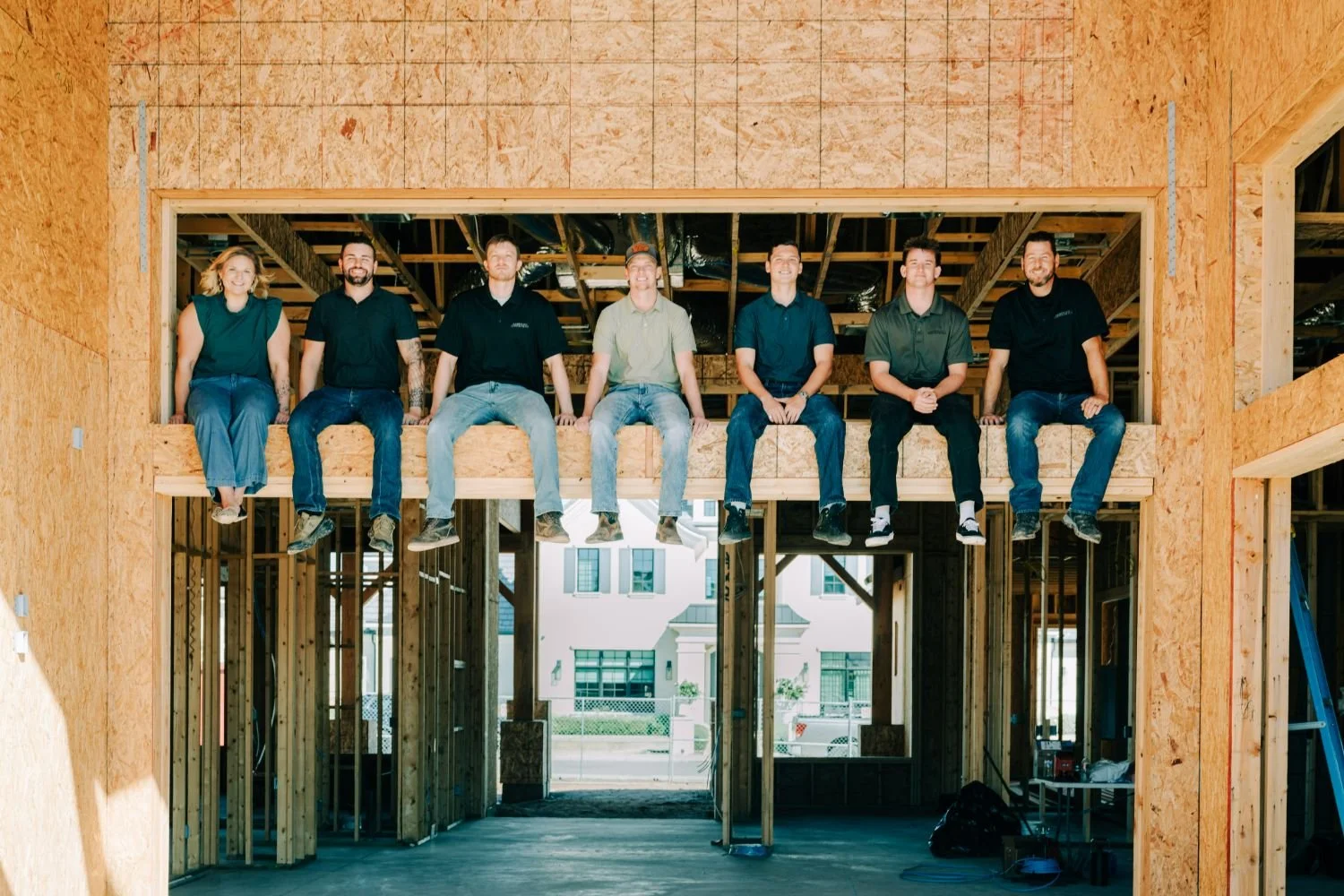 Group of seven diverse construction workers sitting on a beam inside a building under construction.