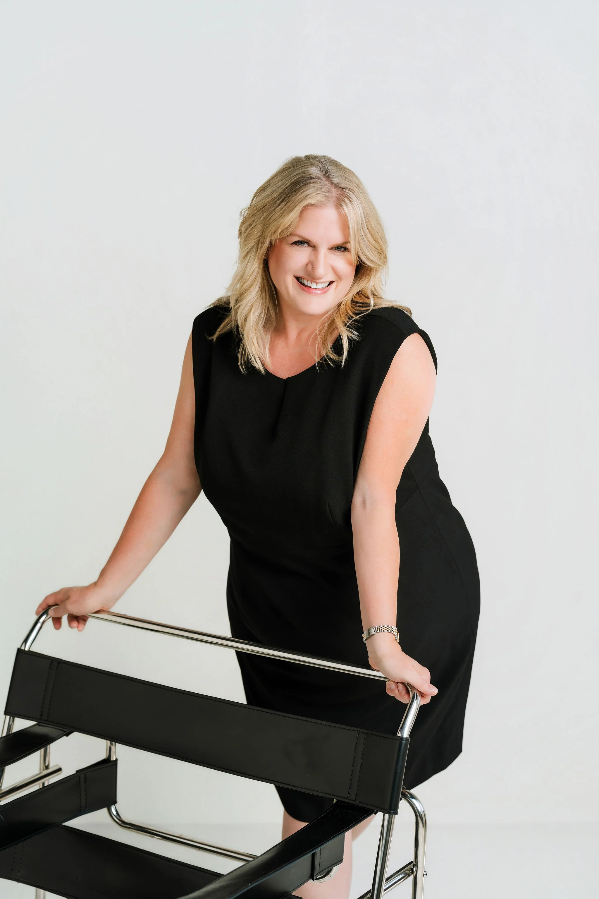 Laurie Clark, Sherwin-Williams Senior Designer Account Executive, smiling in a black dress beside a chrome and leather chair
