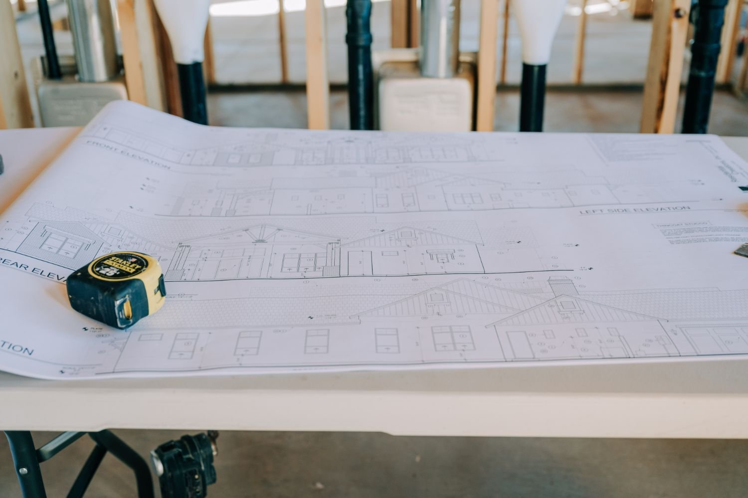 Blueprints spread out on a table at a construction site with a tape measure nearby.