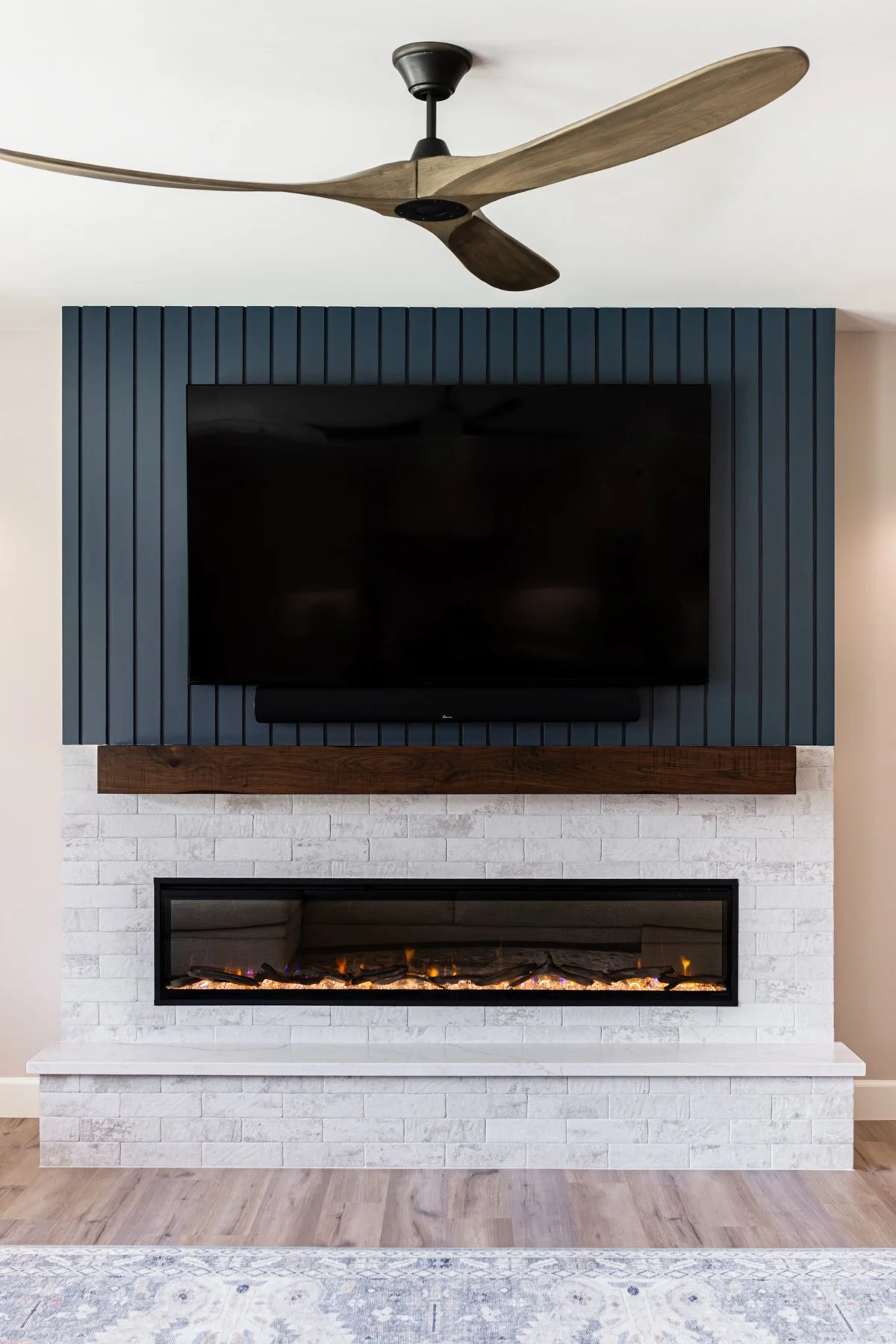 Living room with navy vertical slat accent wall, wood mantel, and white brick linear fireplace showing bold interior paint colors