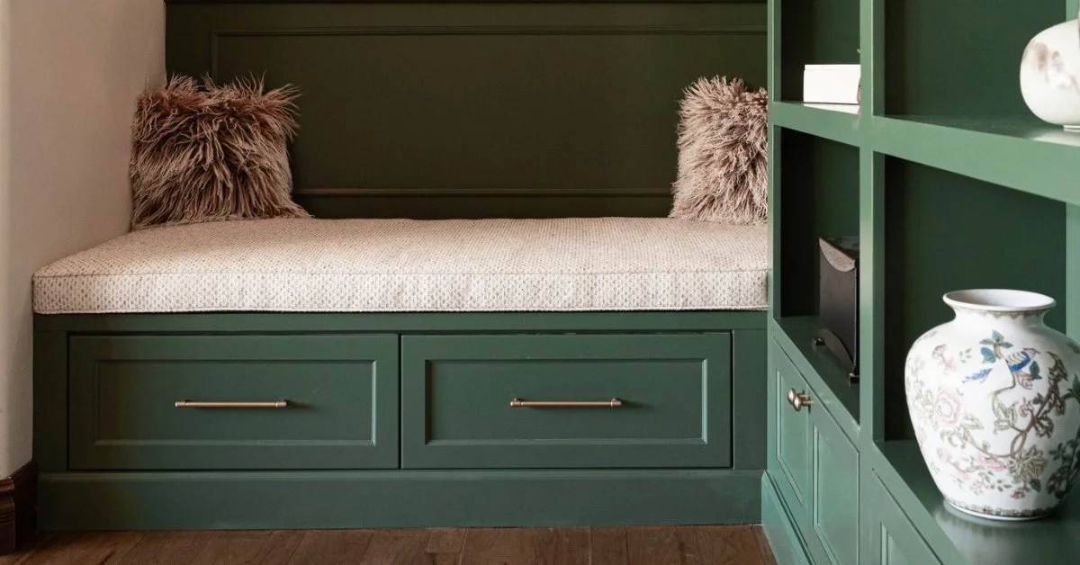 Green painted built-in bench with cushion, brass drawer pulls, and shelving with a floral vase, showing interior paint colors