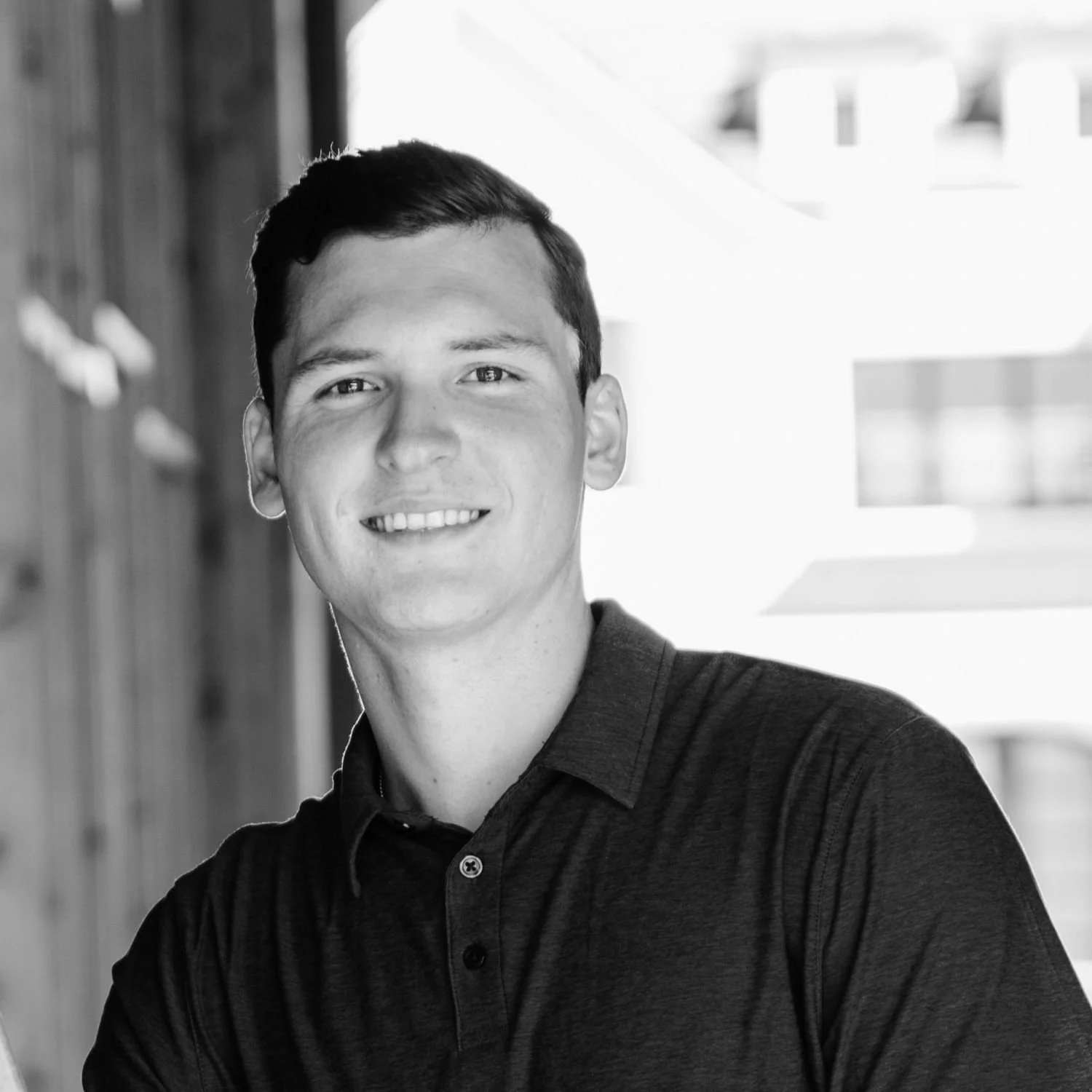 Luke, with a wooden wall and windows in the background.