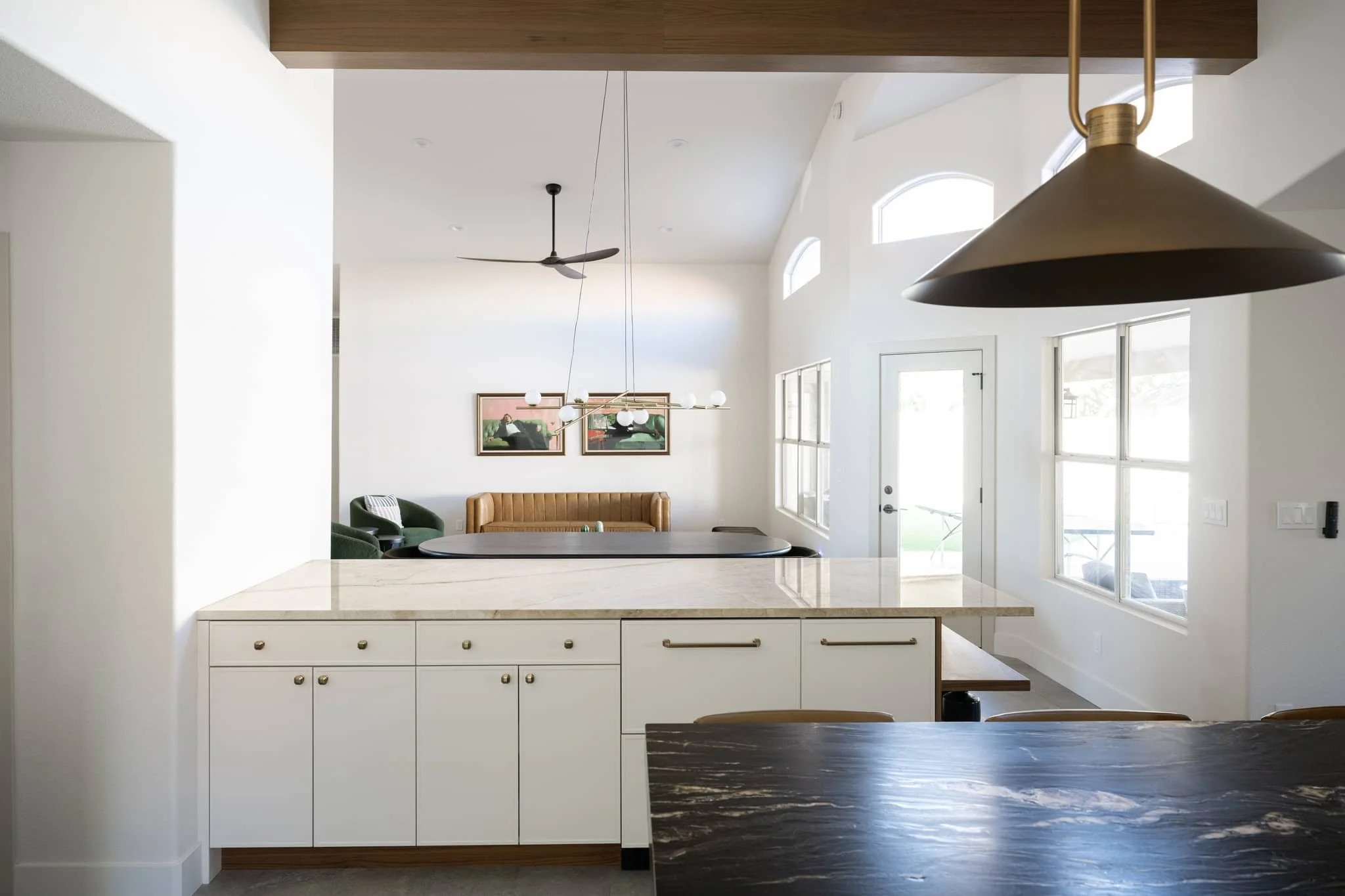 Open-concept kitchen with white cabinets and stone peninsula looking into a dining area and living room with vaulted ceilings