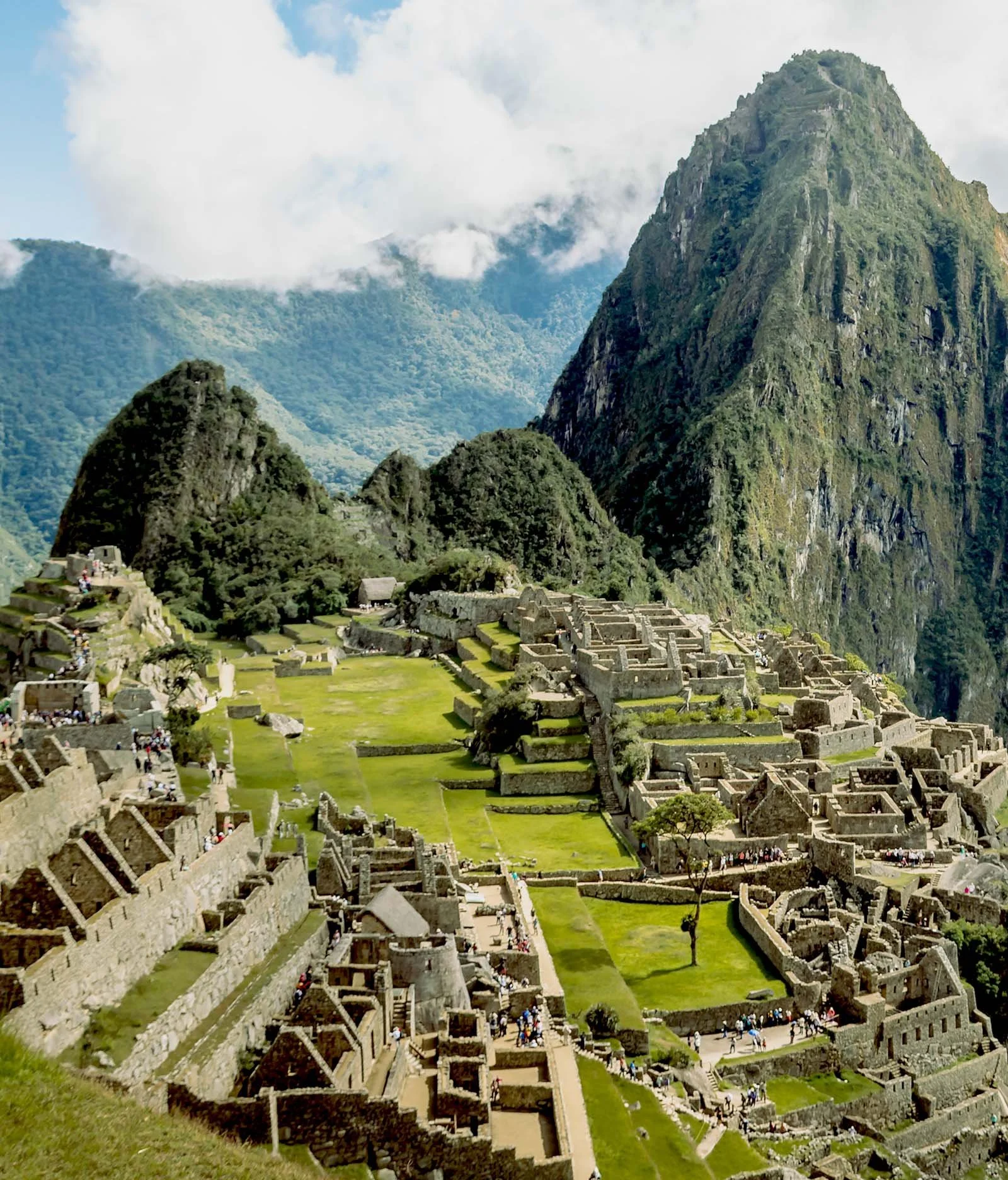 Ancient Incan ruins at Machu Picchu with lush green mountains and cloudy sky in the background.