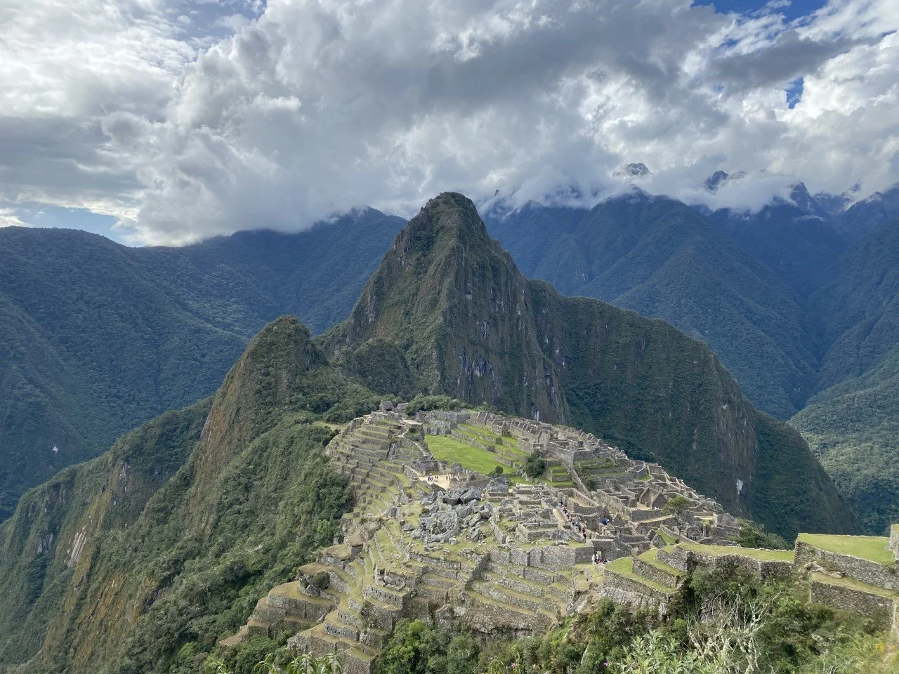 Ancient stone ruins of Machu Picchu on a steep mountain, with lush green vegetation and cloudy skies in the background.