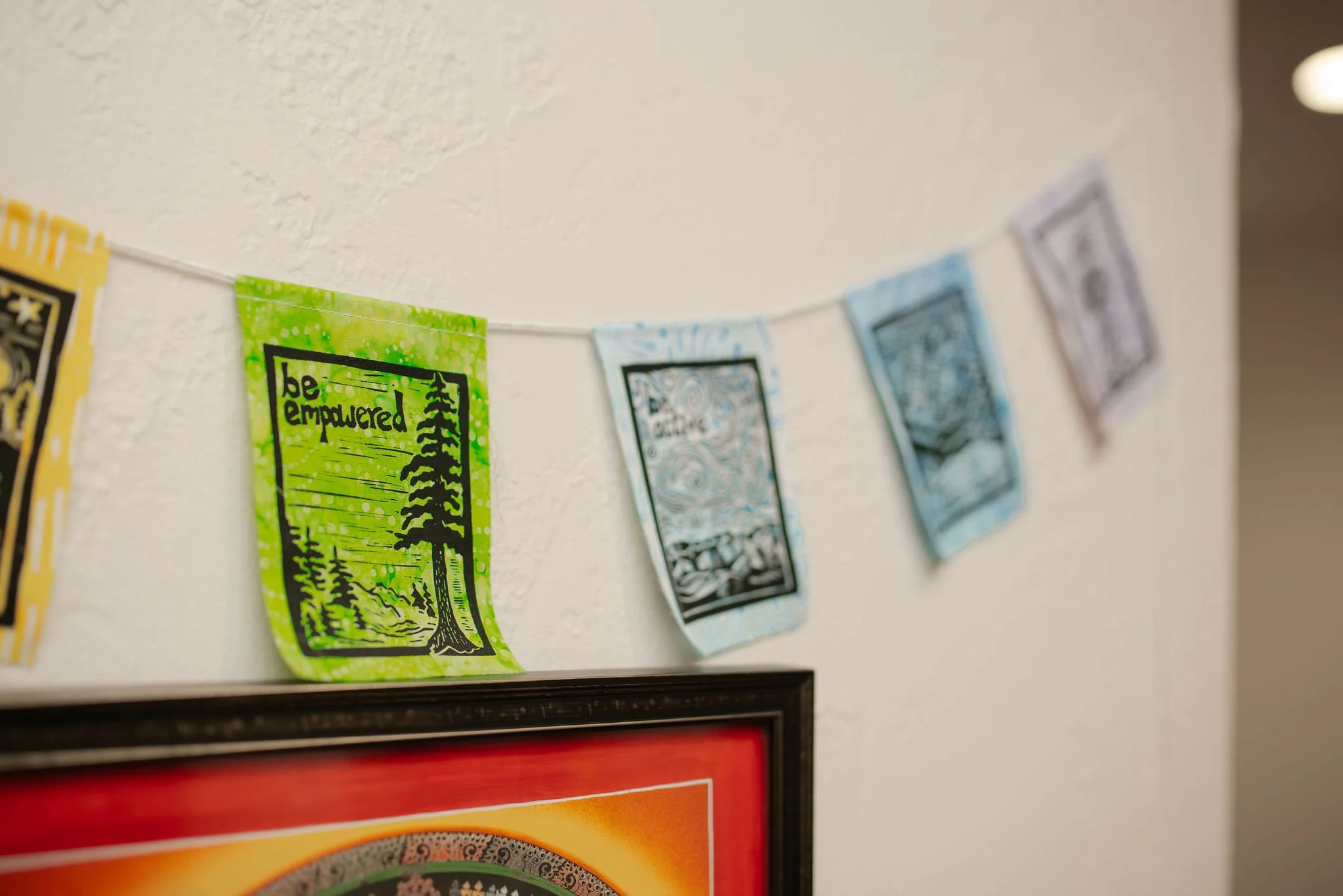 Colorful decorative banners hanging on a string on a wall, with a framed artwork below.