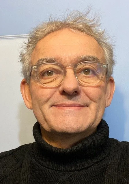 Headshot of male executive with silver hair and glasses smiling and looking directly into the camera