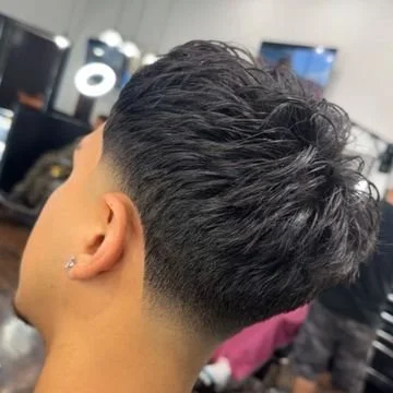 Close-up of a man's head with a faded undercut hairstyle, longer curly hair on top, and an earring in his ear