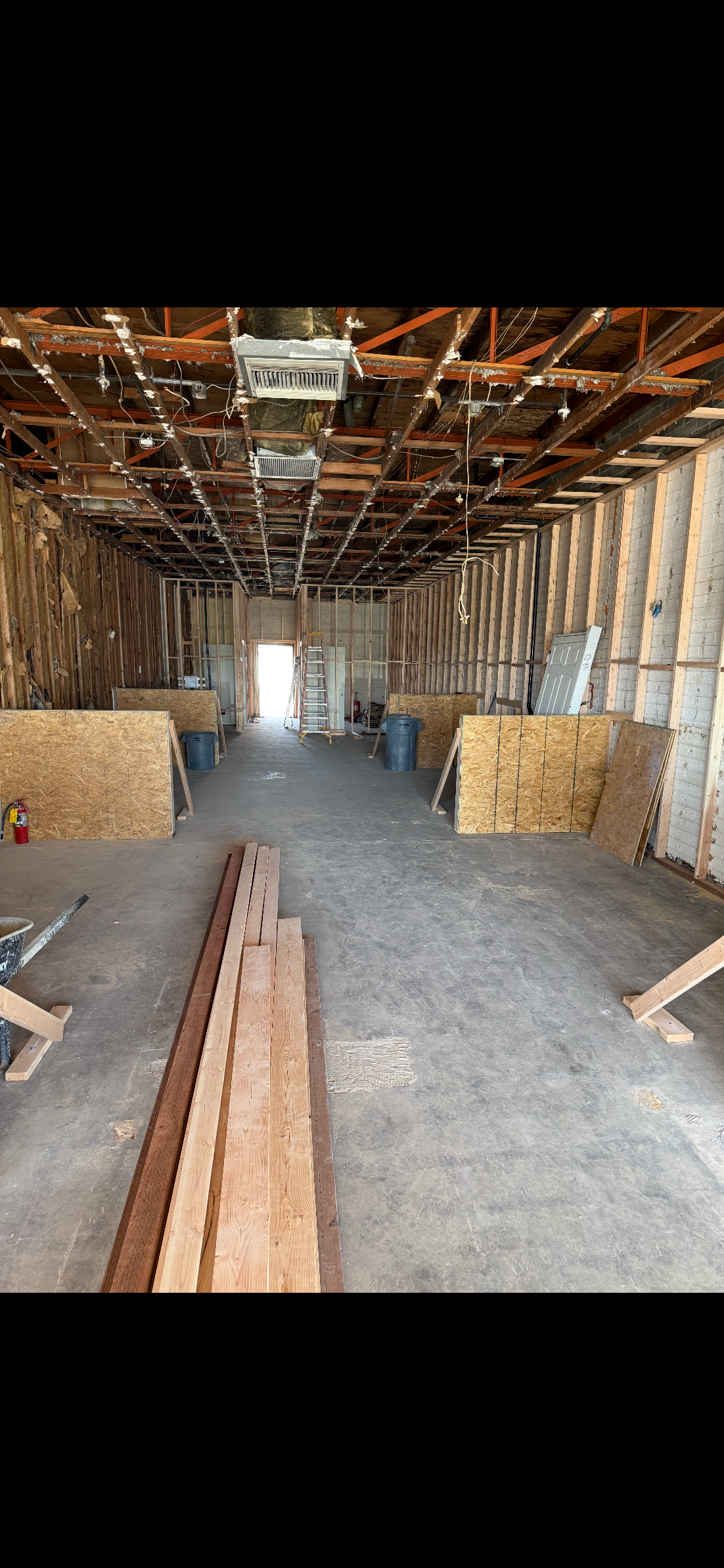 Interior of a building under construction or renovation with exposed ceiling structure, construction materials, and tools.