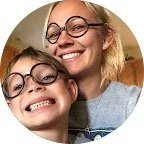 Two smiling women with glasses, close together, in a cozy indoor setting.