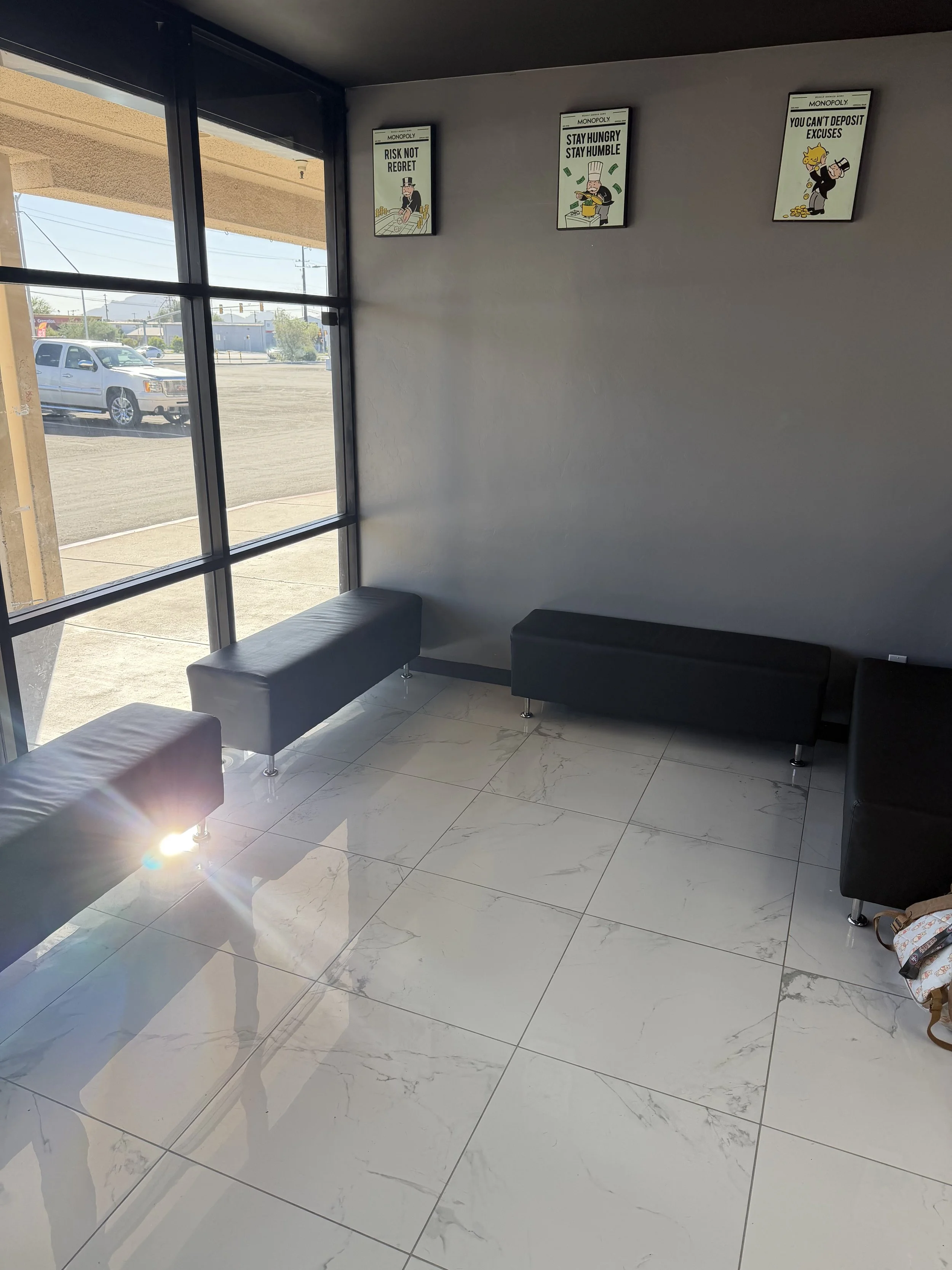 Empty waiting area with a large window, black benches, and three motivational posters on the wall.