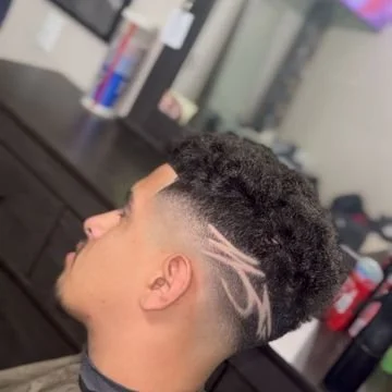 Side profile of a young man with a short curly hairstyle featuring a shaved design with white lines.