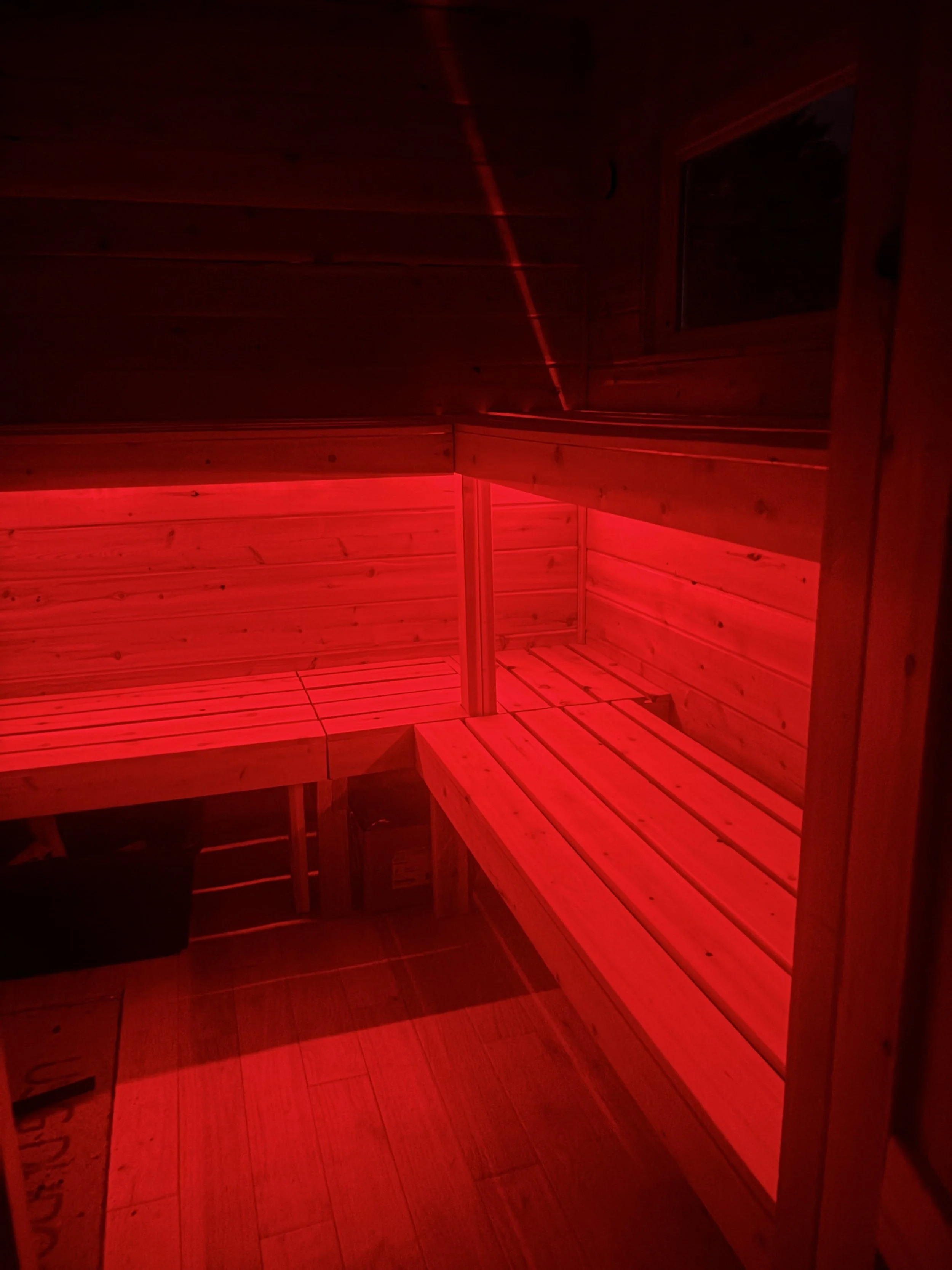 Inside a wooden sauna with benches illuminated by red light.