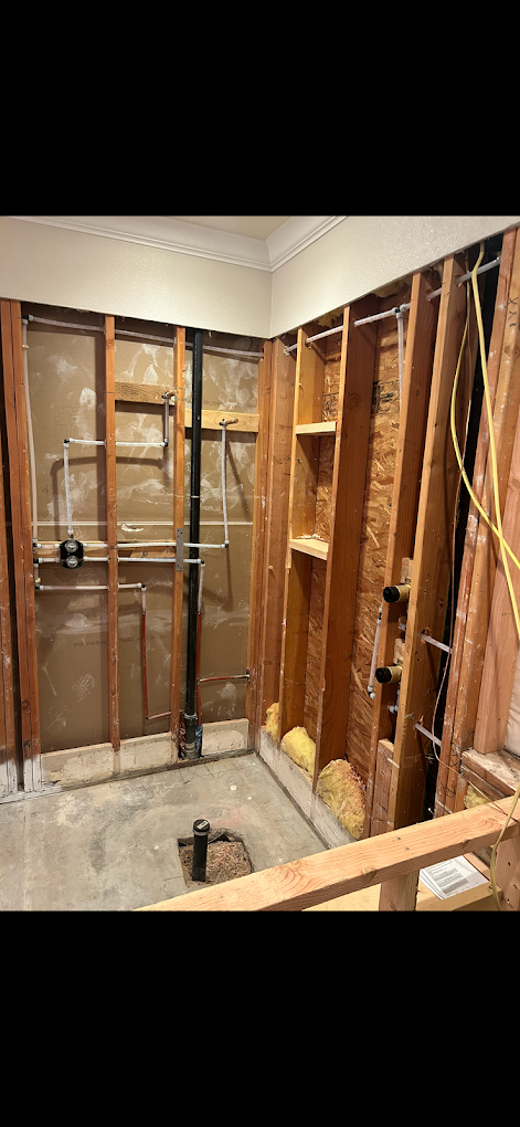 Partially renovated bathroom with exposed wall studs, plumbing, and insulation, ongoing renovation work.