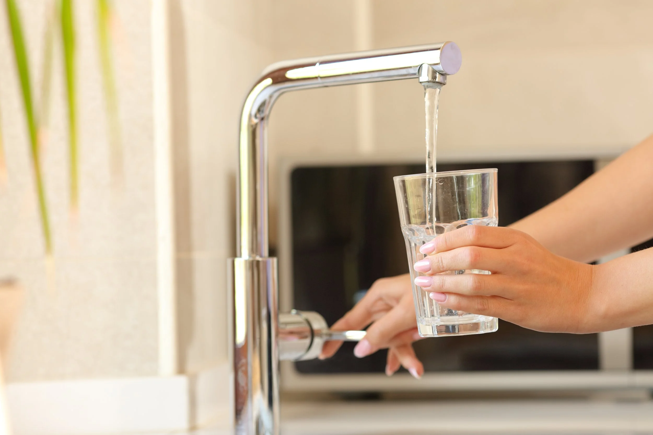 Person filling a glass with water from a kitchen faucet.