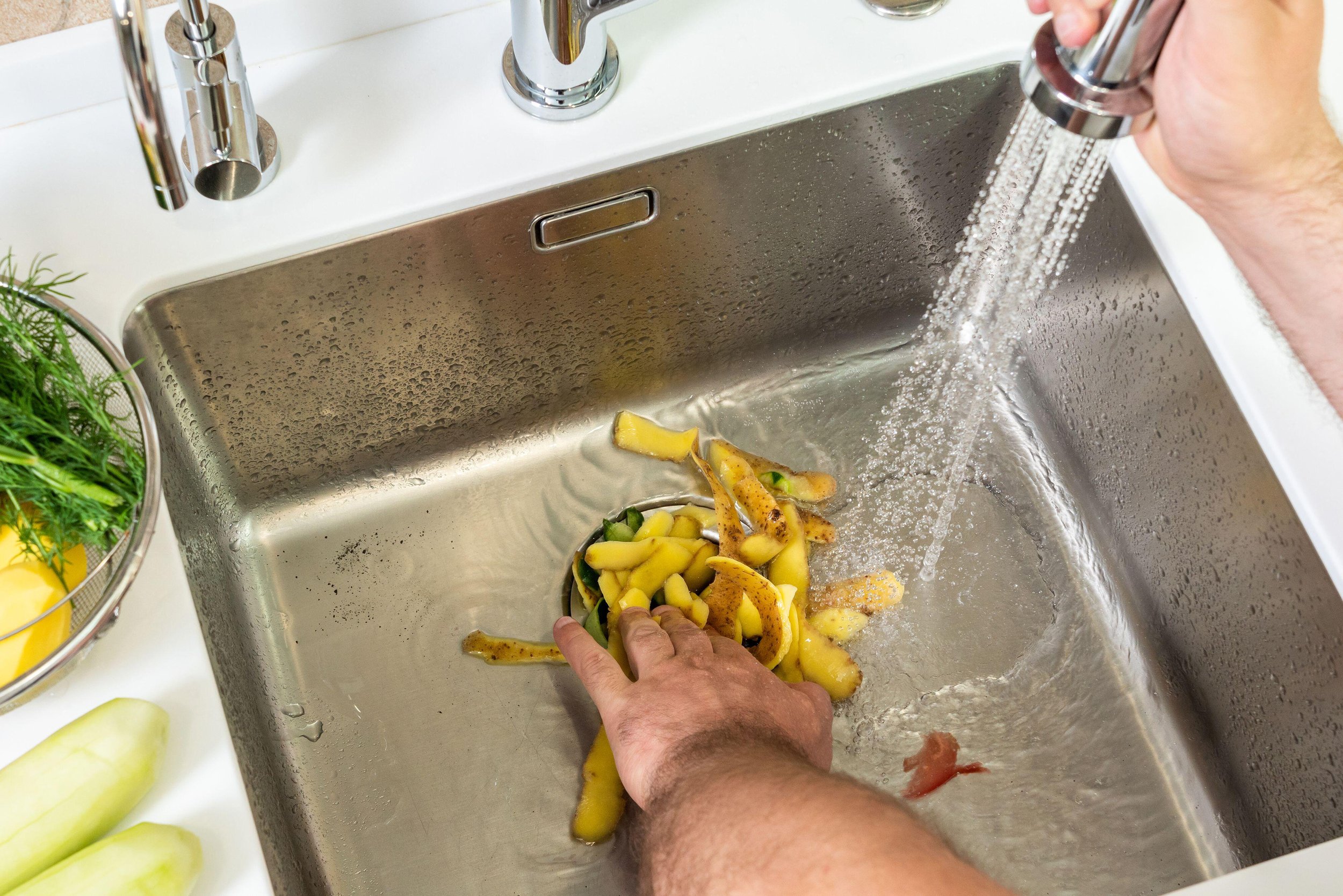 Person rinsing yellow bell peppers under a kitchen faucet in a stainless steel sink.