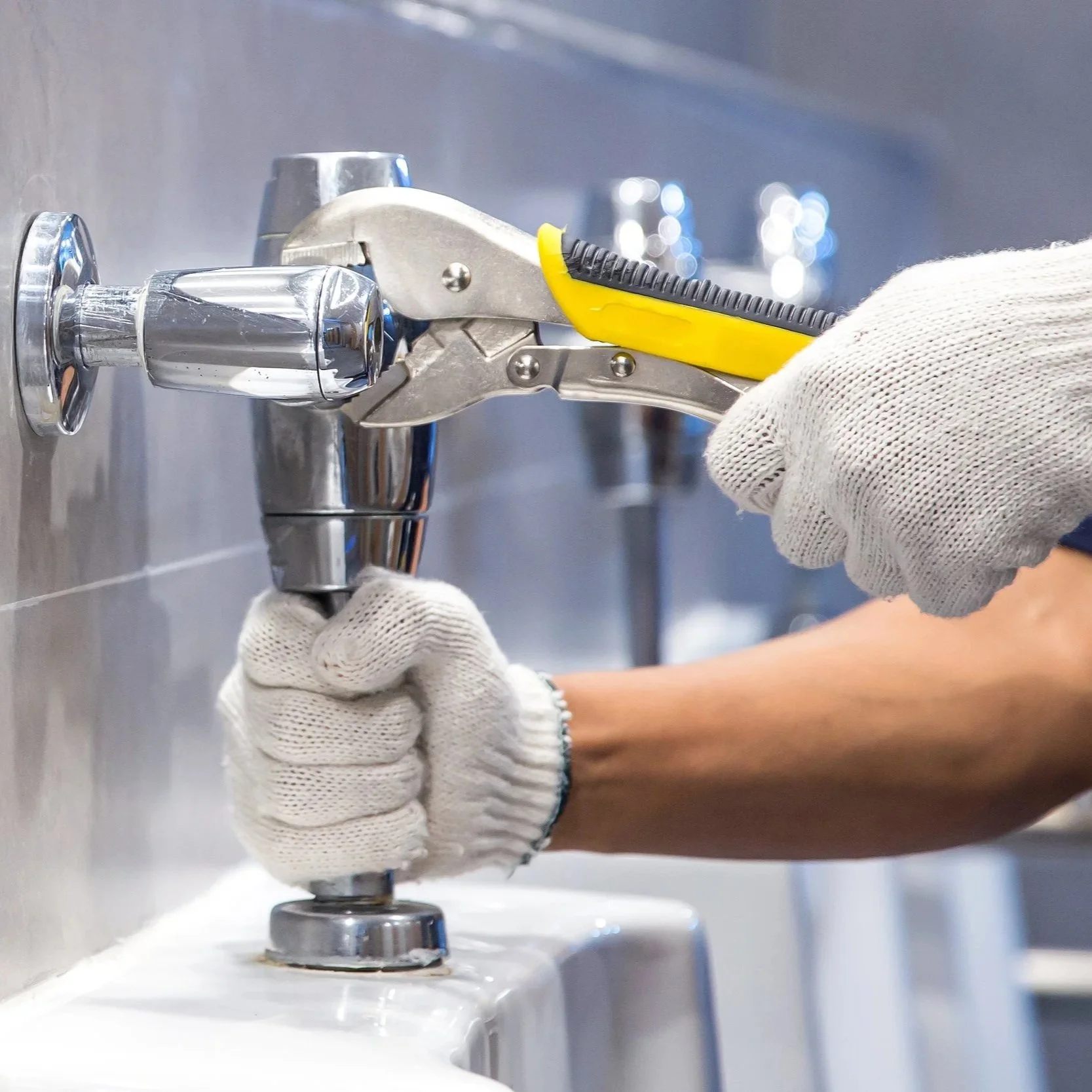 A person repairing a sink using pliers and a wrench, wearing white gloves.