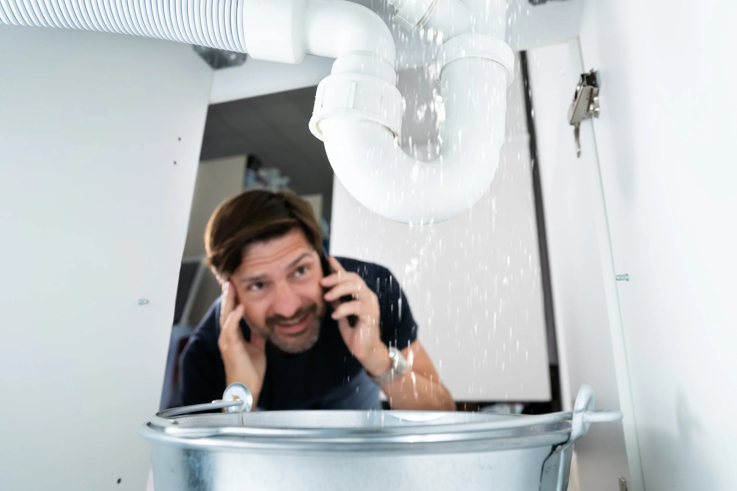 guy calling plumber looking at a leaking pipe