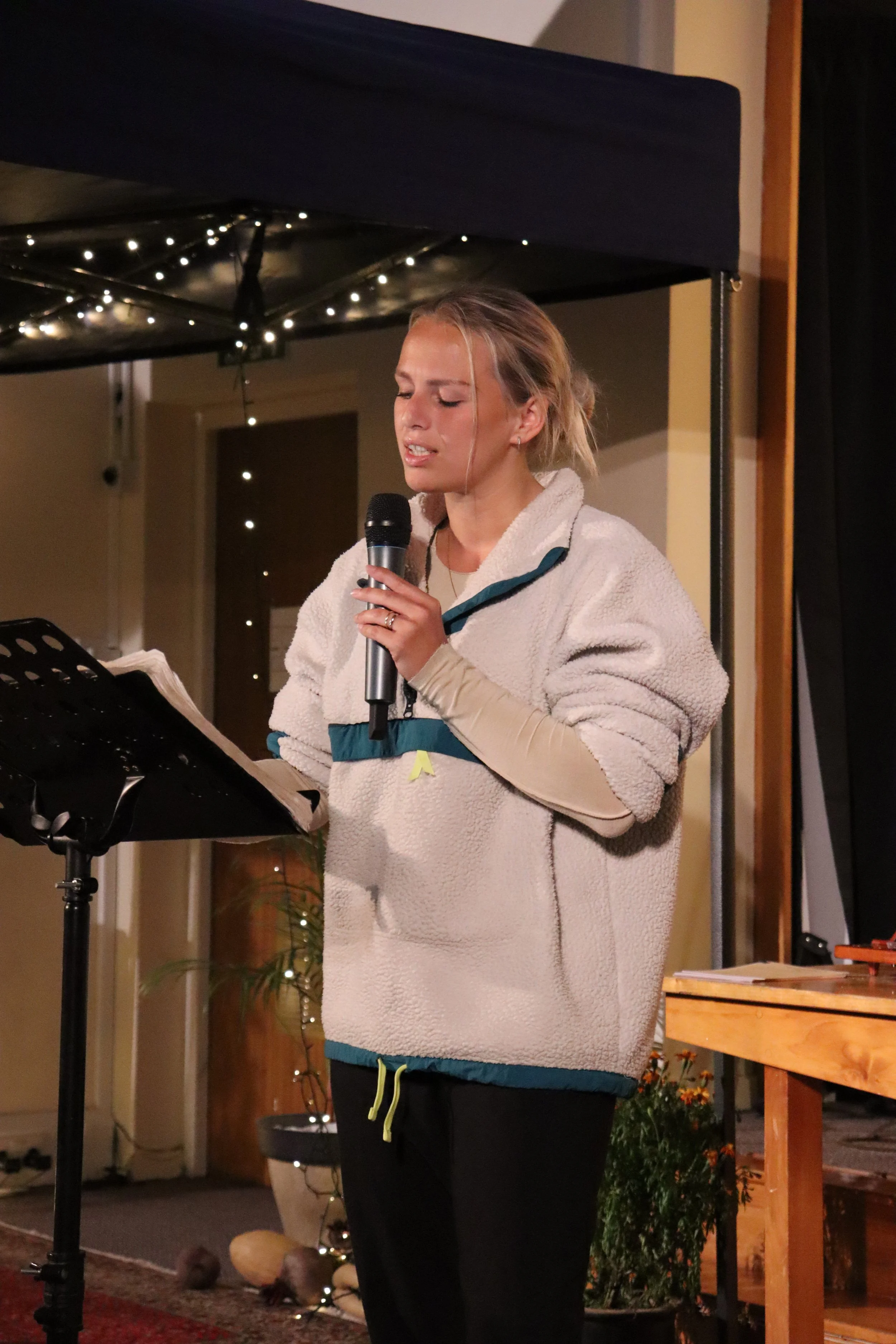 A woman with blond hair preaching with a microphone in an indoor setting, in a church.