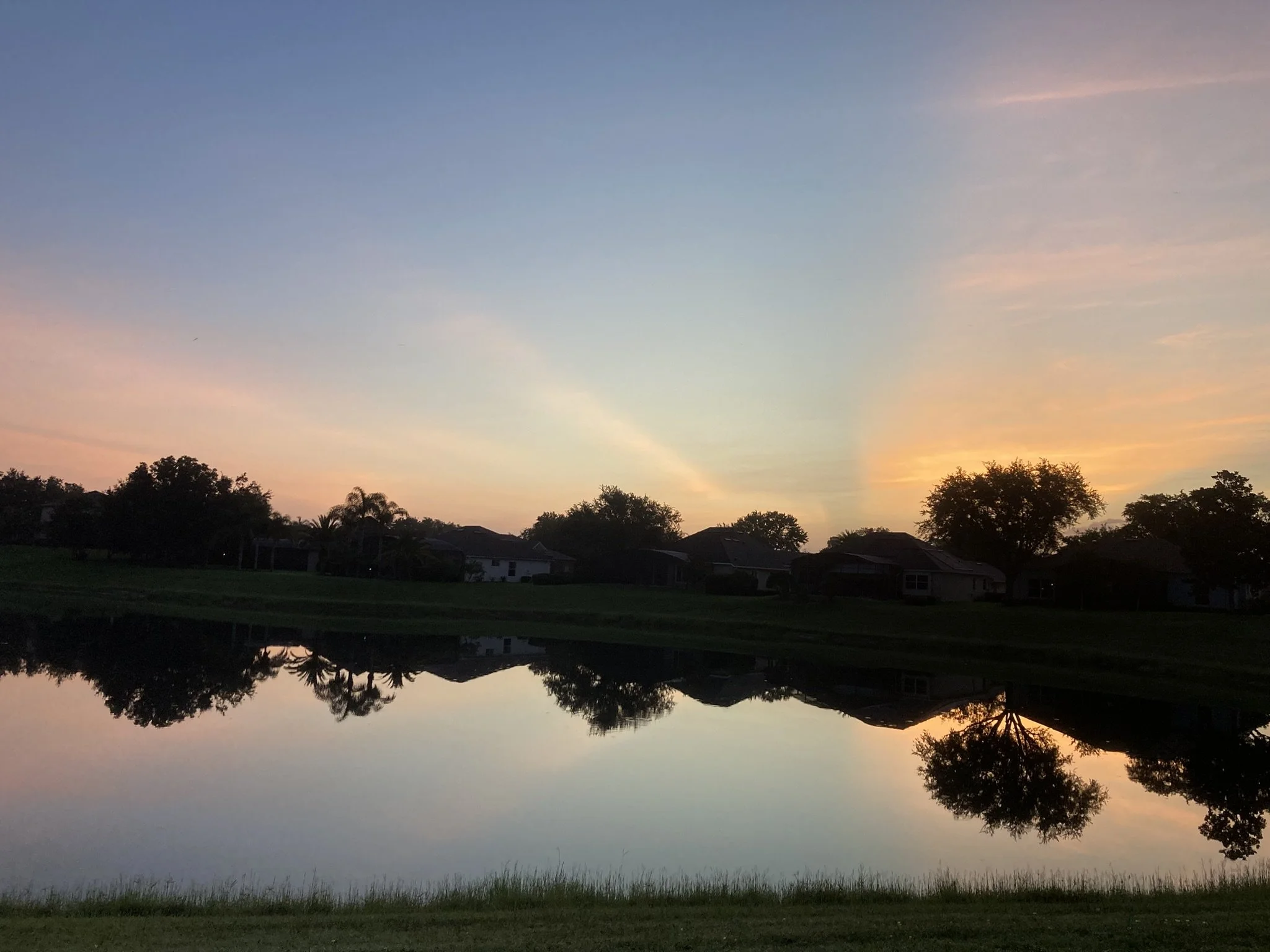 Sunrise sun rays across the sky with trees reflecting on the water