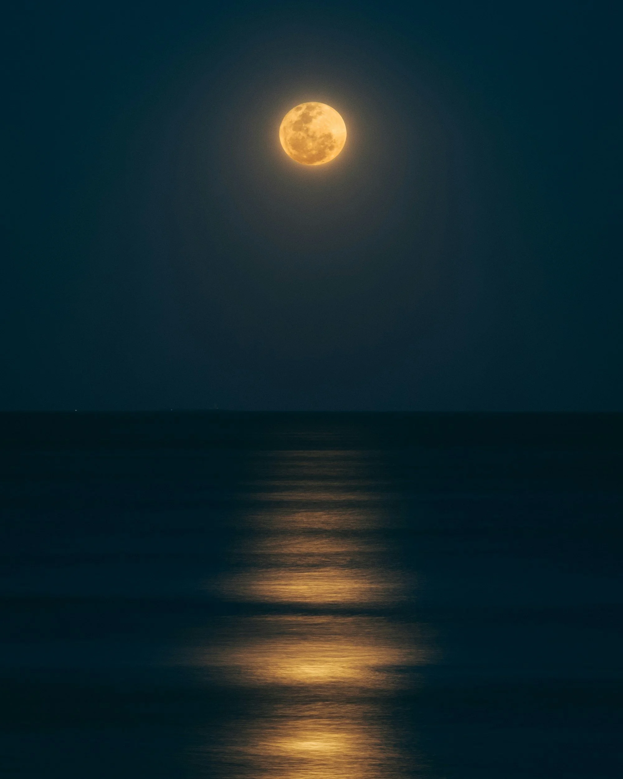 Full moon over the ocean at night with its reflection on the water.