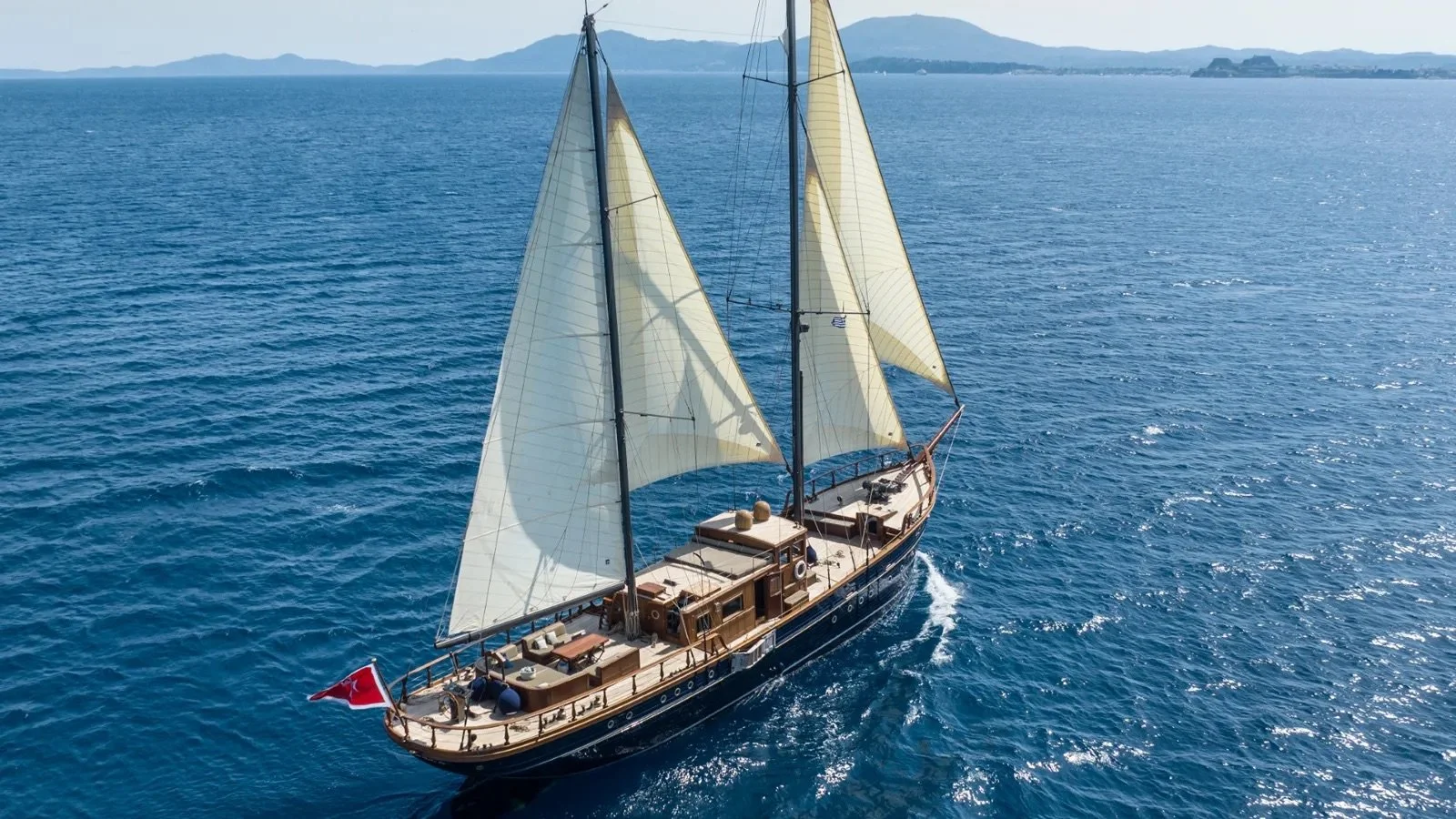 A drone footage of a luxury sail yacht with beige sails sailing around Corfu, Greece.