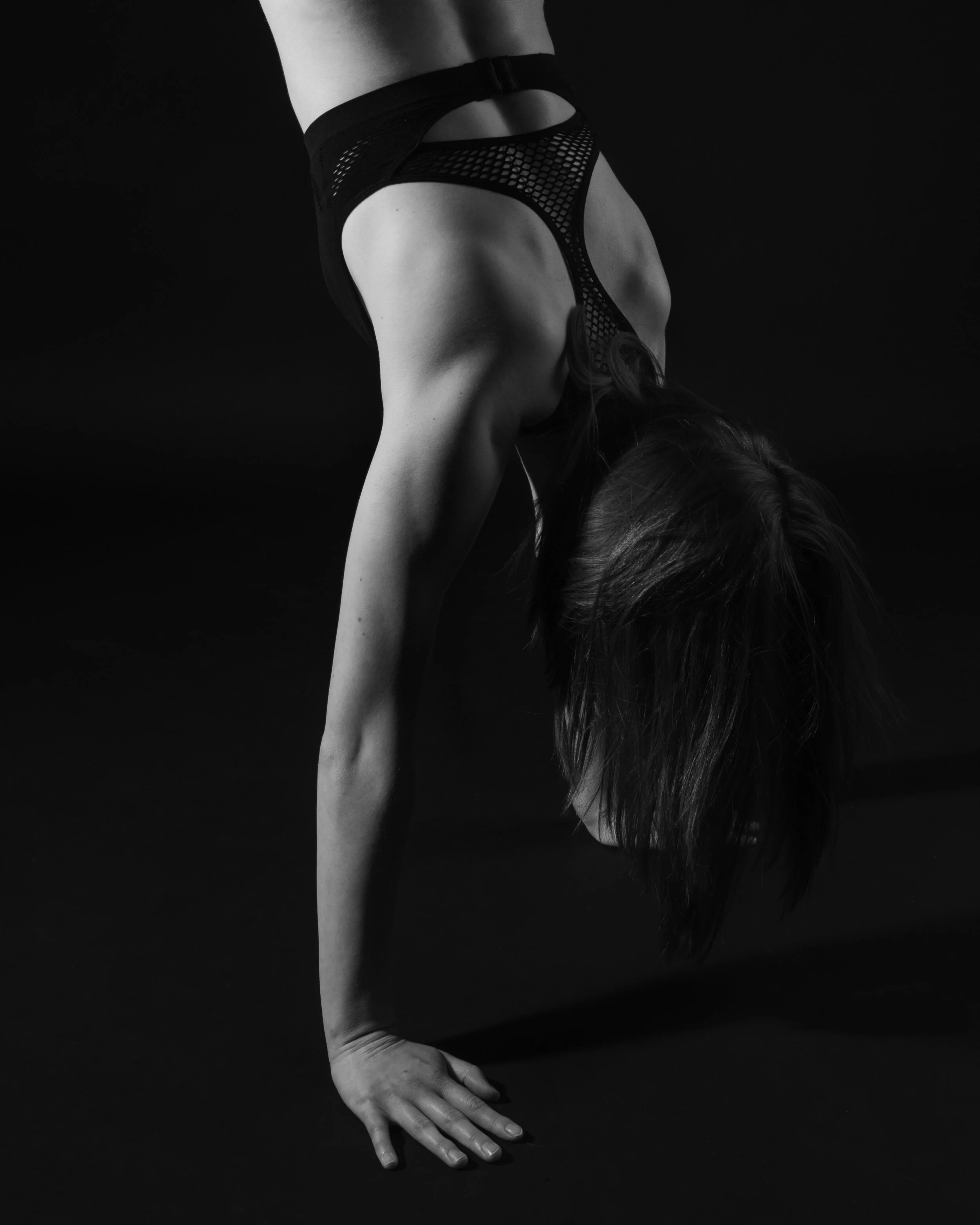 A person performing a downward dog yoga pose, wearing black fishnet clothing in a dark setting.