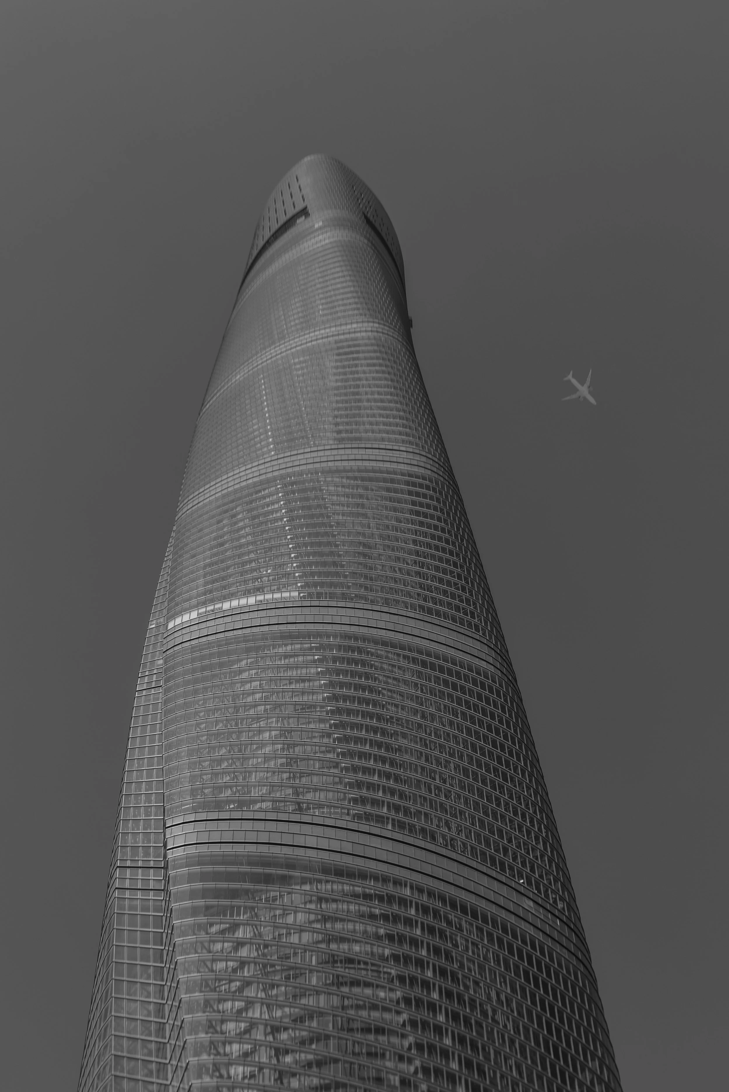 A tall, modern skyscraper viewed from below, with an airplane flying in the sky nearby.