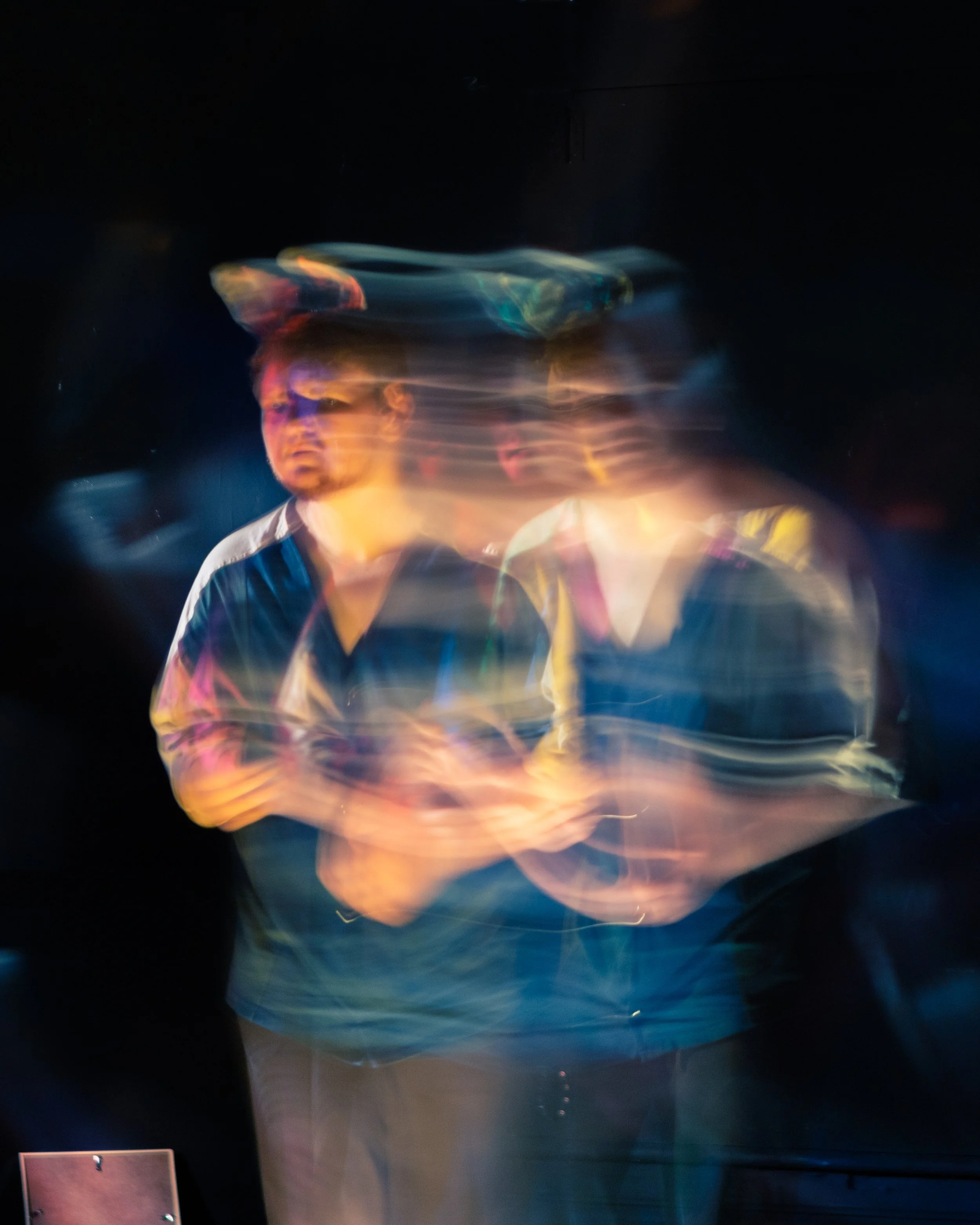 Two men with blurred motion and light trails in a dark setting, standing close together.