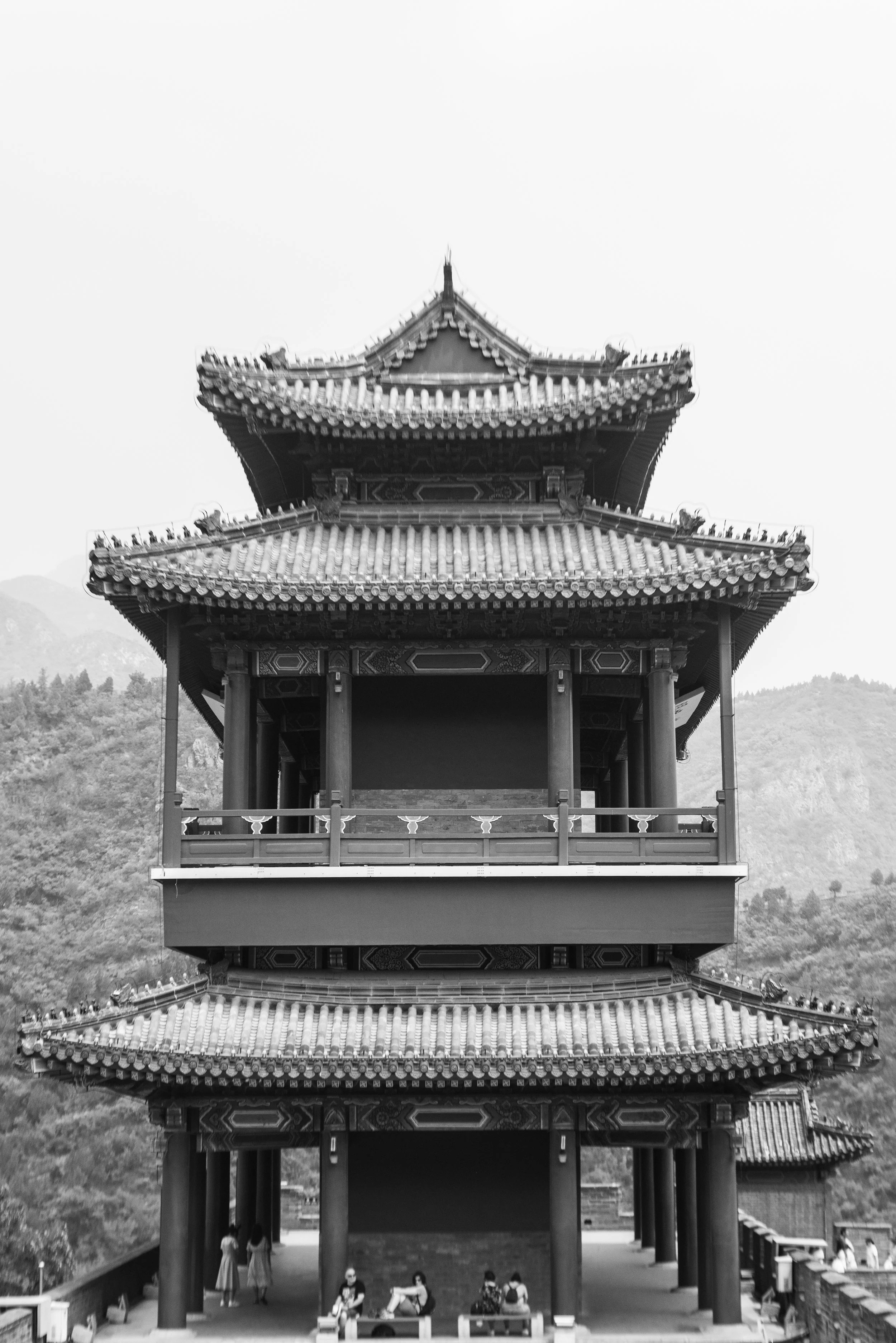 Black and white photo of a traditional Chinese pagoda with multiple tiers, intricate architectural details, and a mountainous landscape in the background.