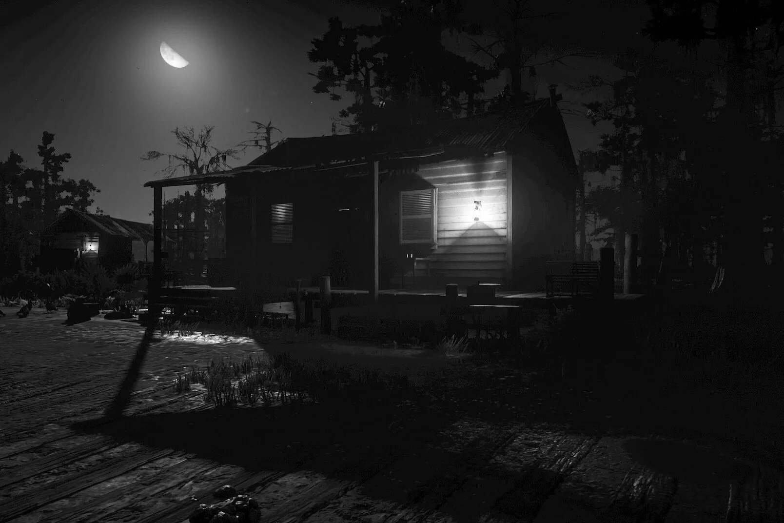 A black and white photo of a wooden house in a forested area at night, illuminated by a single exterior light, with a moon in the sky, and trees in the background.
