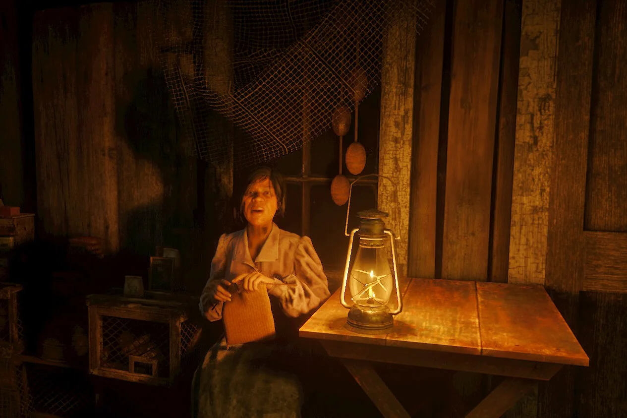 A woman with short dark hair sitting in a rustic wooden room, illuminated by a lantern on a wooden table, with a worried or scared expression on her face.