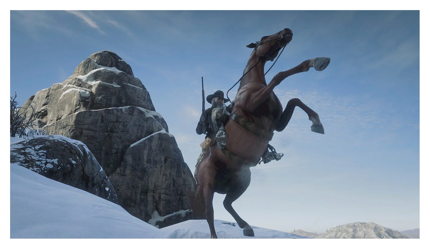 A cowboy riding a rearing horse in a snowy mountainous landscape with large rocks and a blue sky.