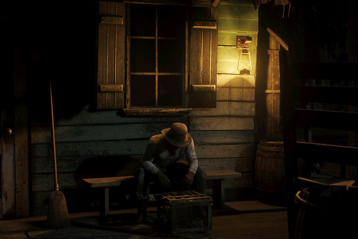 A dimly lit porch scene with a figure wearing a wide-brimmed hat sitting on a bench next to a crate, with a broom leaning against the wall nearby. There's a large barrel on the right and a window with shutters above the figure. A lantern is mounted o