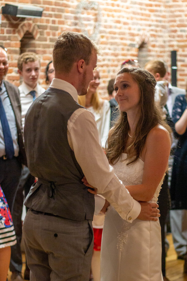 Bride and groom dancing at their wedding reception with guests watching in a brick-walled venue.