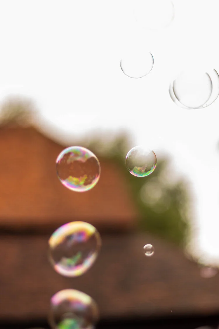 Soap bubbles floating outdoors in front of a blurred background of a house and trees.