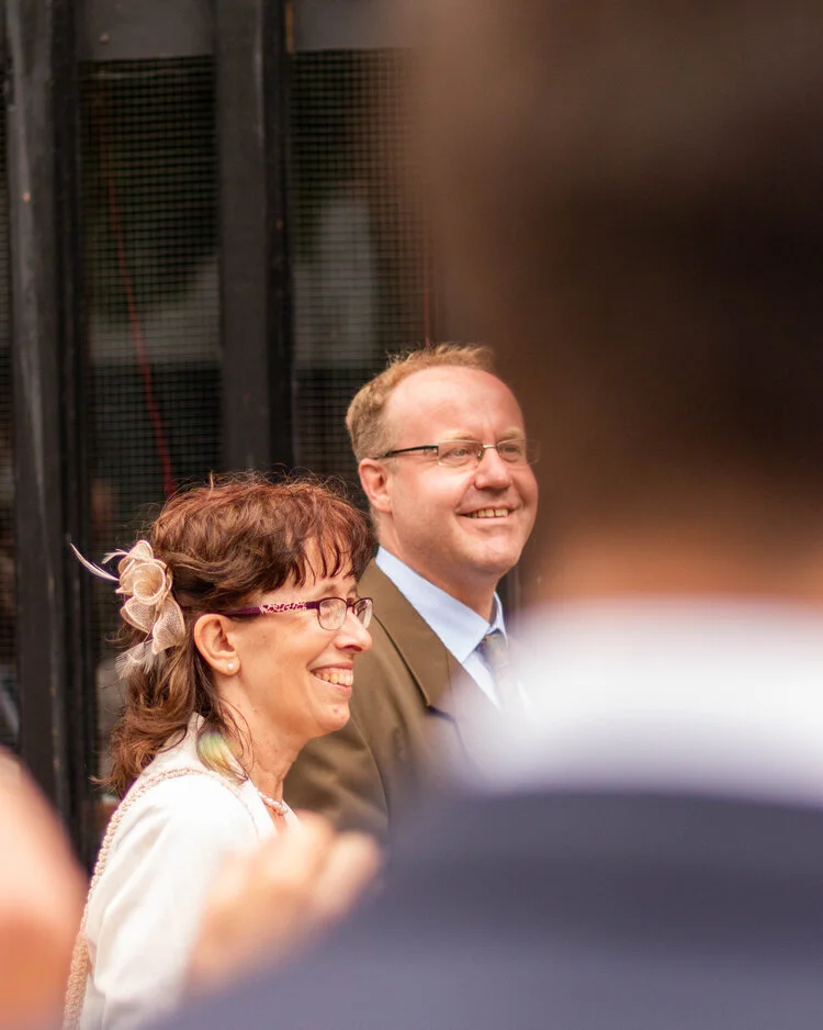 Smiling woman with glasses and a man in a suit at an event.