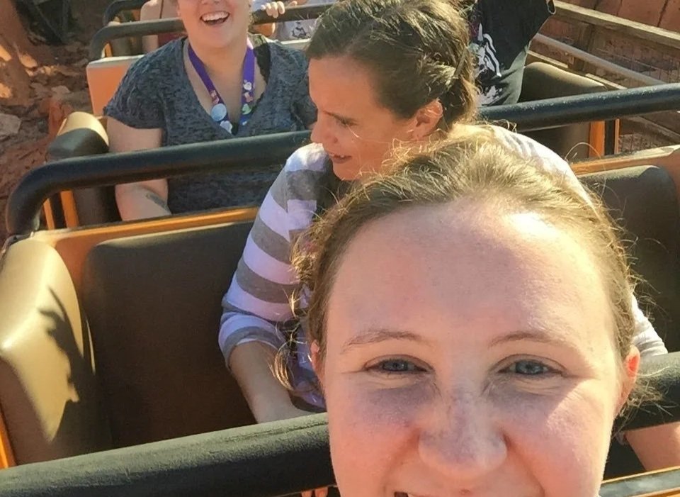 Four people riding a roller coaster amusement park ride, smiling and enjoying the experience.