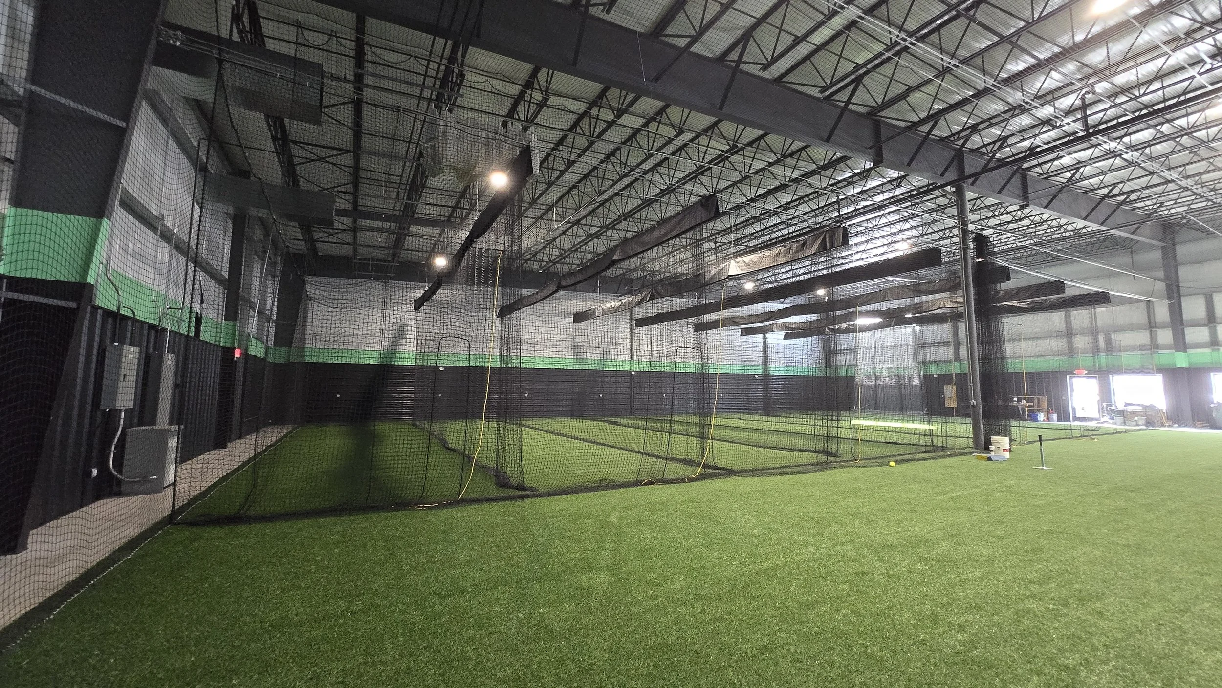 PWR FASTPITCH Indoor baseball or softball training facility with a turf field, batting cages, and netting.