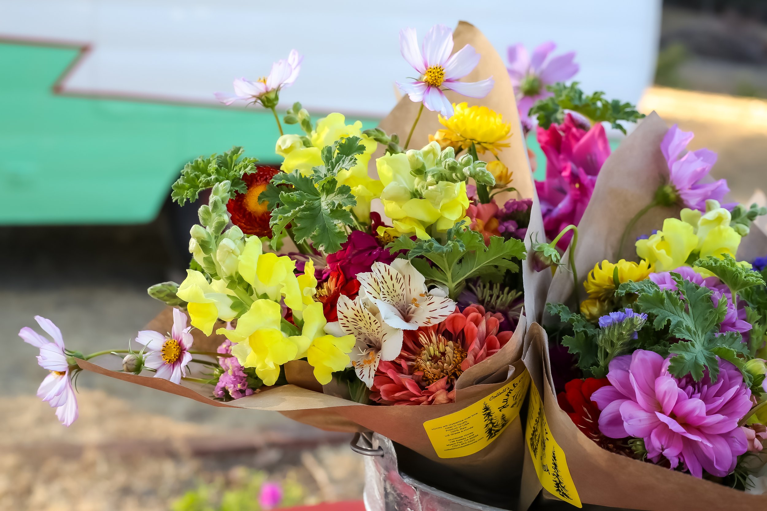 Colorful bouquets of fresh flowers including yellow, pink, and purple blooms wrapped in brown paper on a metal container.